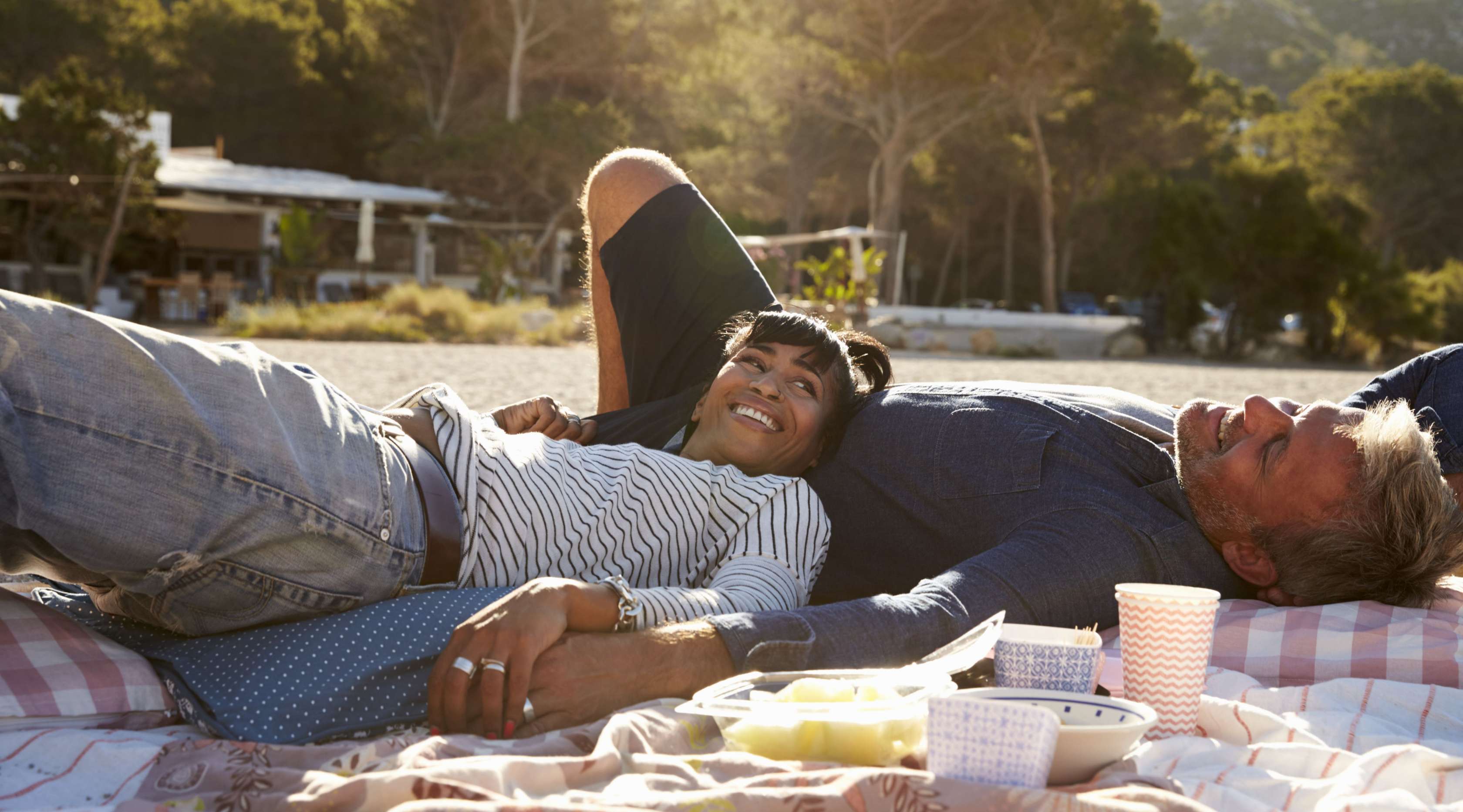 Paar liegt am Strand auf einer Picknick-Decke und macht ein Picknick