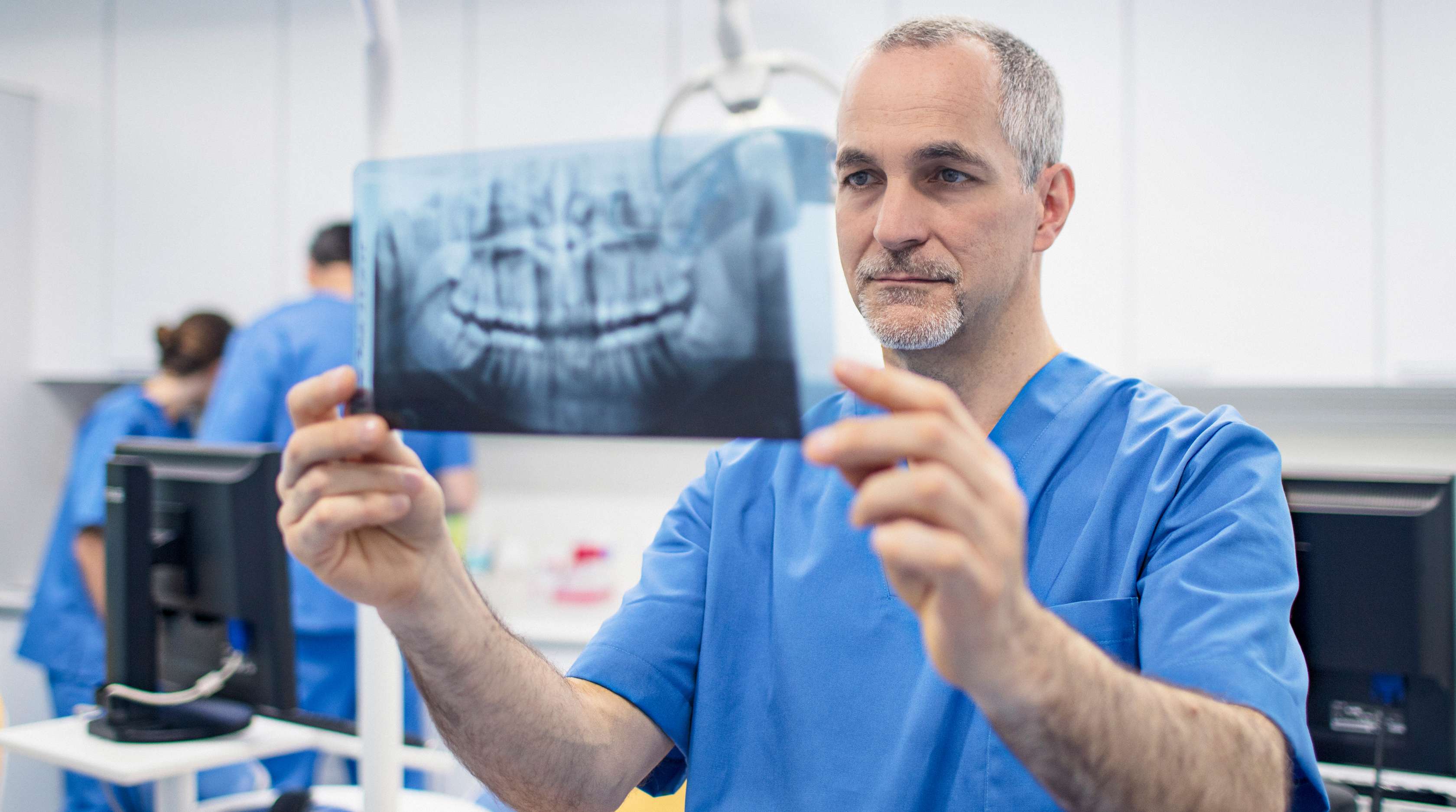 Zahnarzt hält ein Röntgenbild eines Kiefers vor sich und schaut darauf