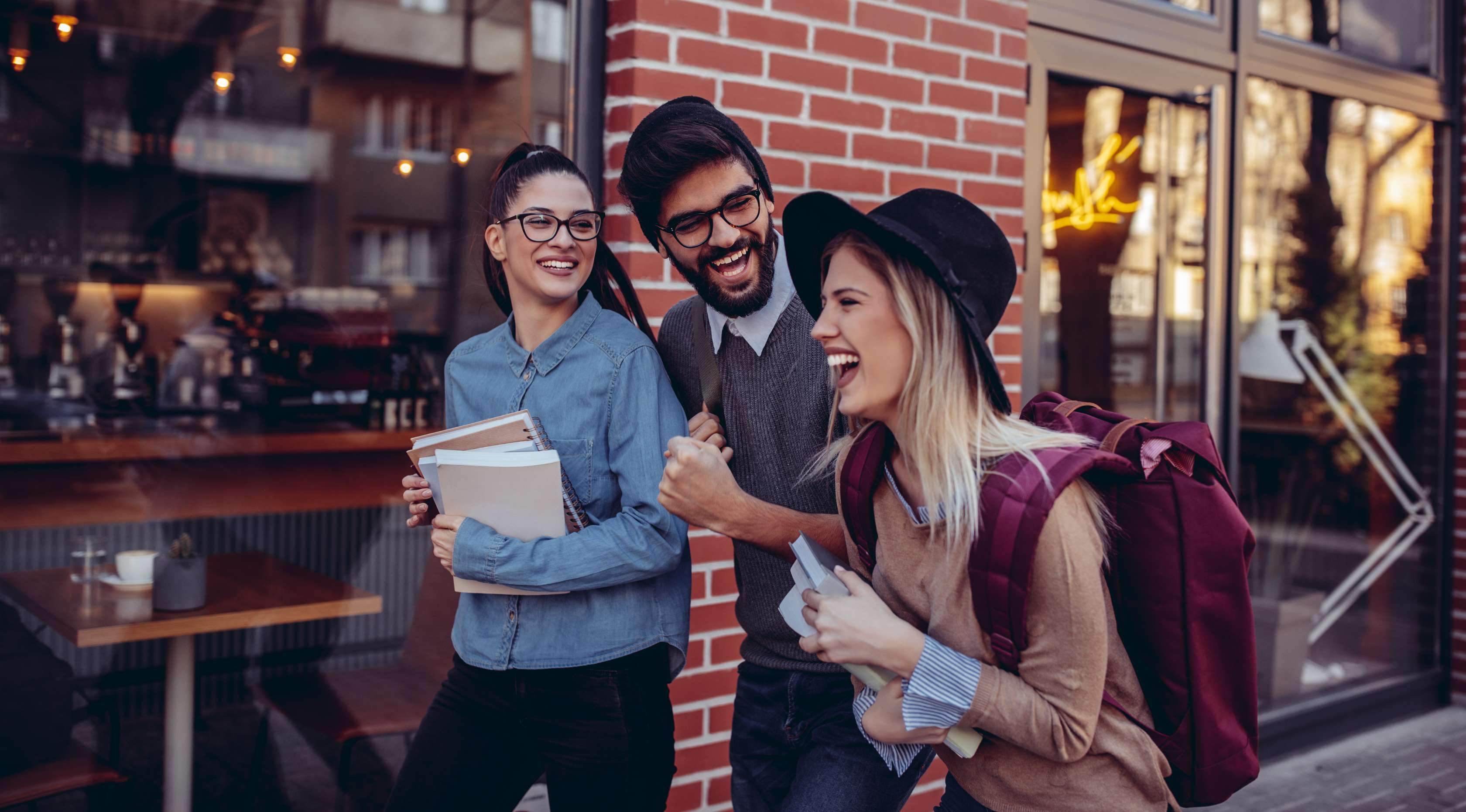 Drei Studenten gehen an einem Café vorbei und lachen zusammen
