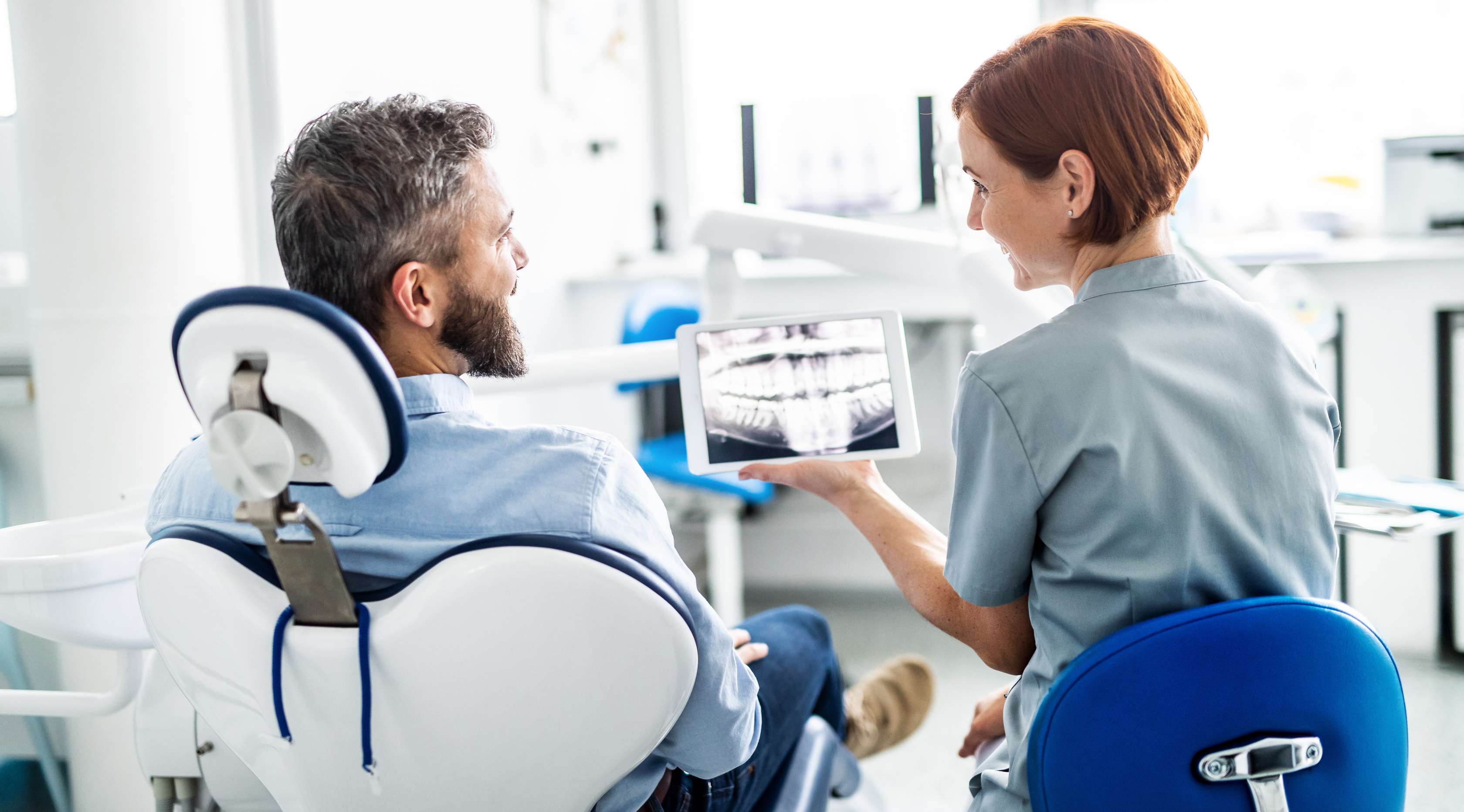 Zahnärztin zeigt Patient auf Behandlungsstuhl eine Röntgenaufnahme seines Gebisses