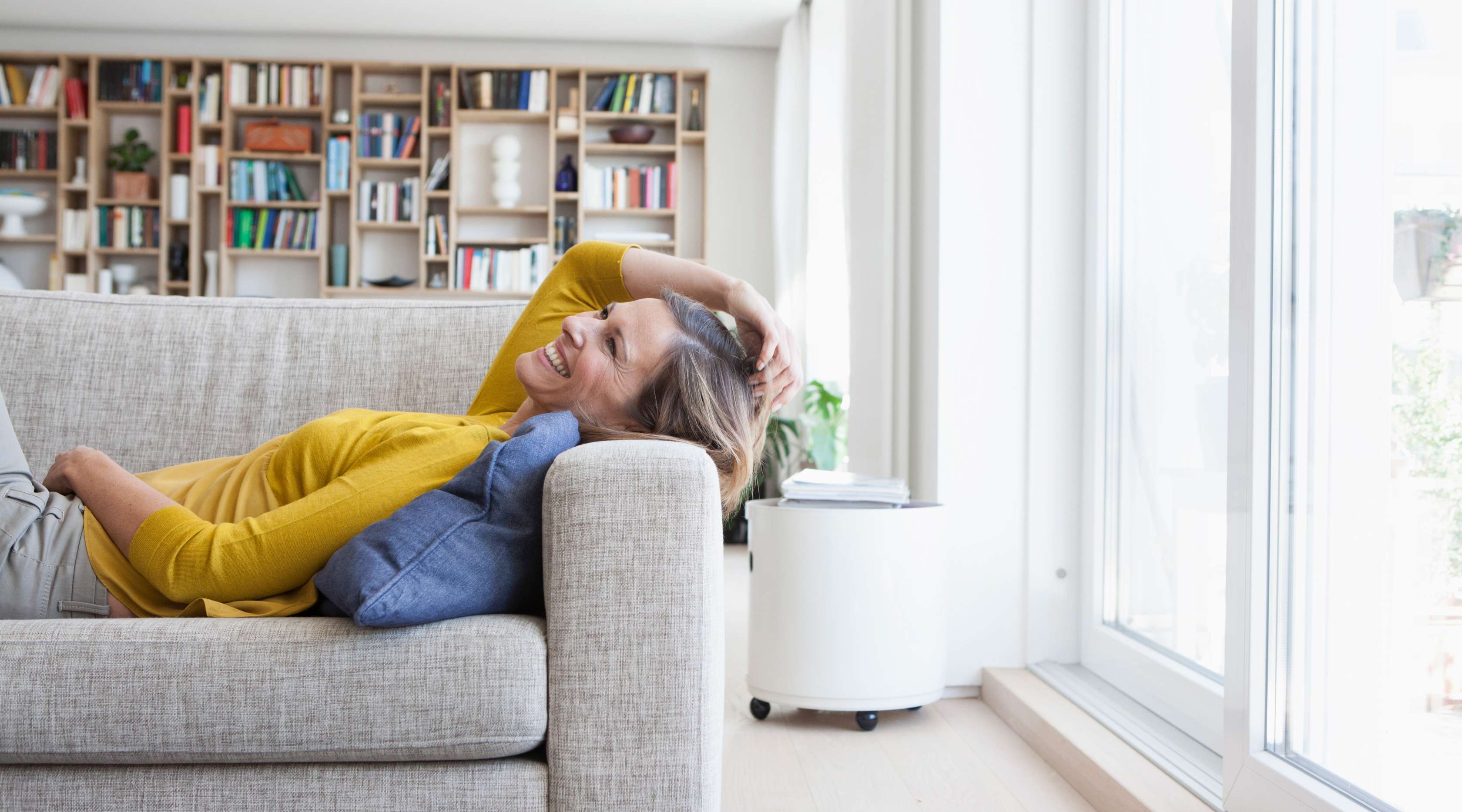 Allianz - Haus- und WohnungsschutzbriefPlus: Frau entspannt, lächelnd im Wohnzimmer auf dem Sofa