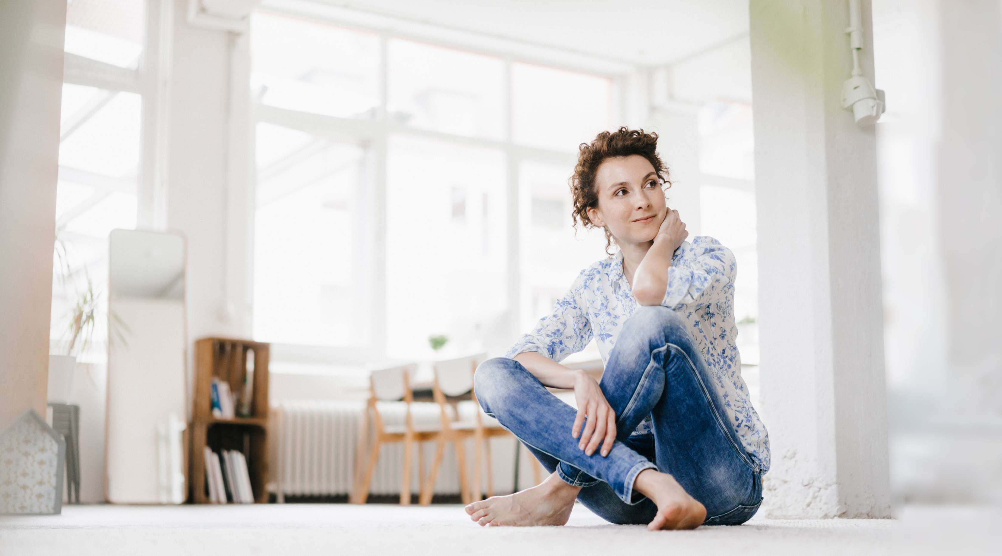 Eine Frau sitzt zuhause auf dem sauberen Fußboden und lächelt