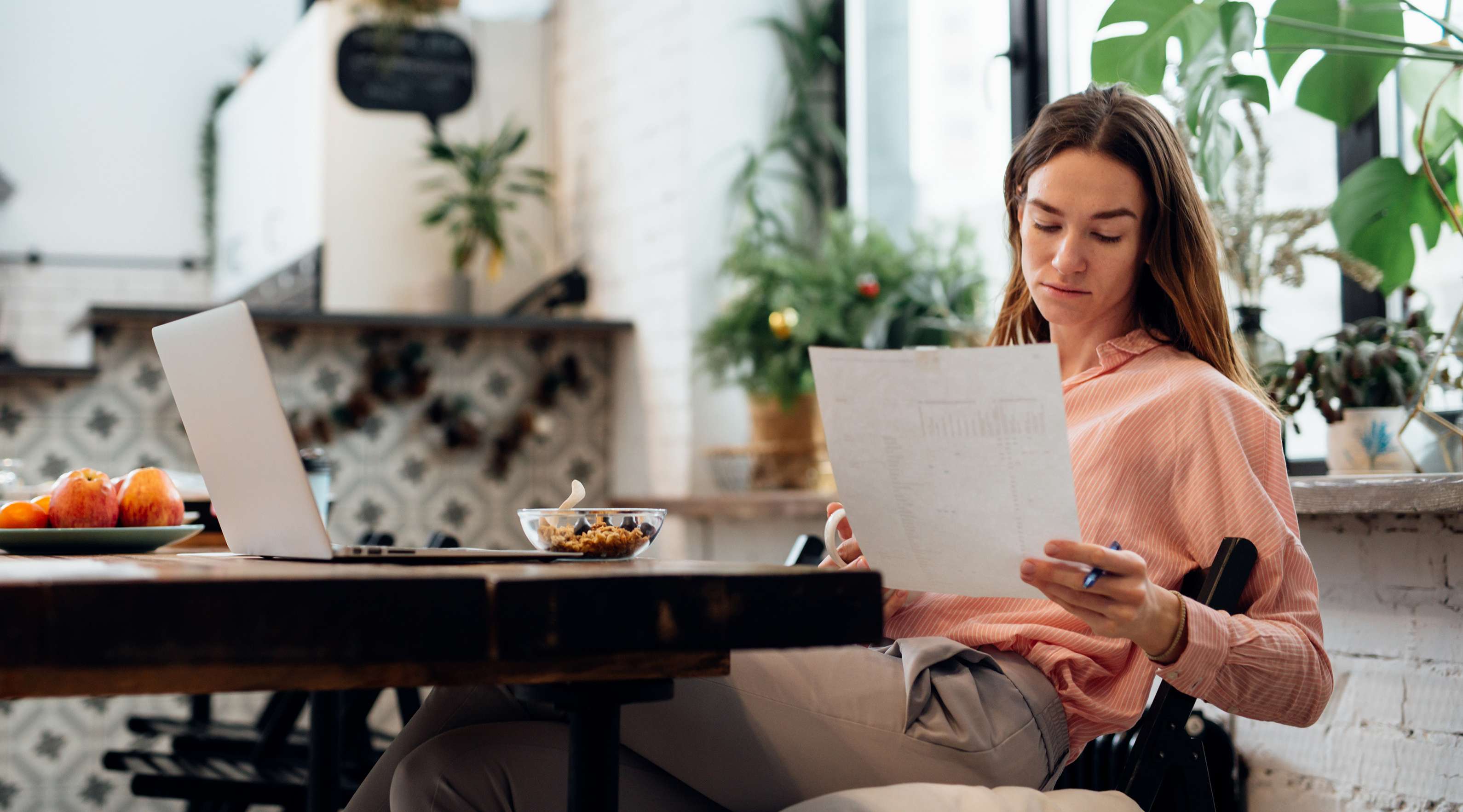 Eine junge Frau sitzt an ihrem Küchentisch und liest ein Dokument