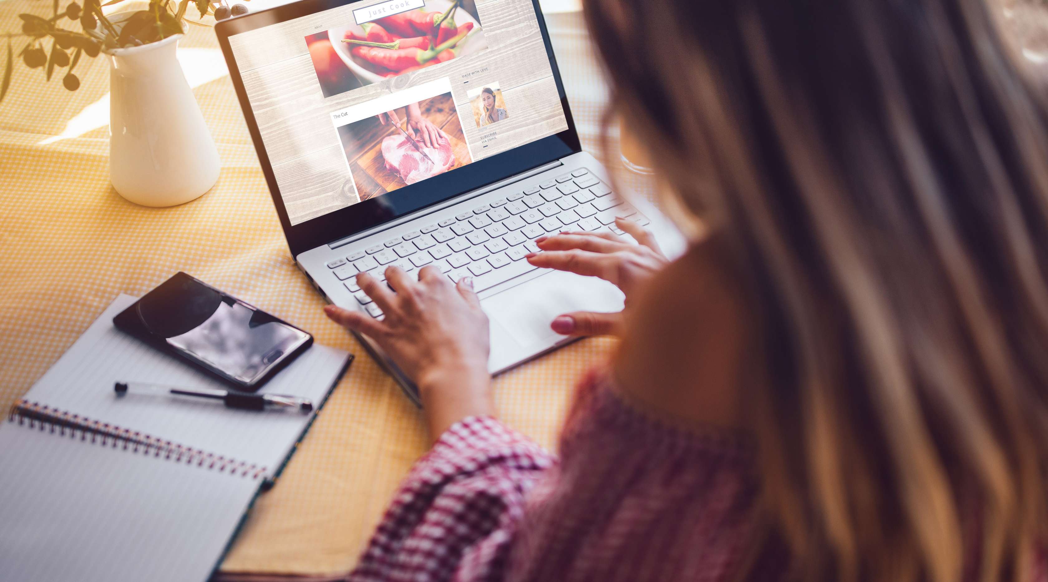 Eine junge Frau sitzt vor dem Laptop und schreibt an ihren Food-Blog