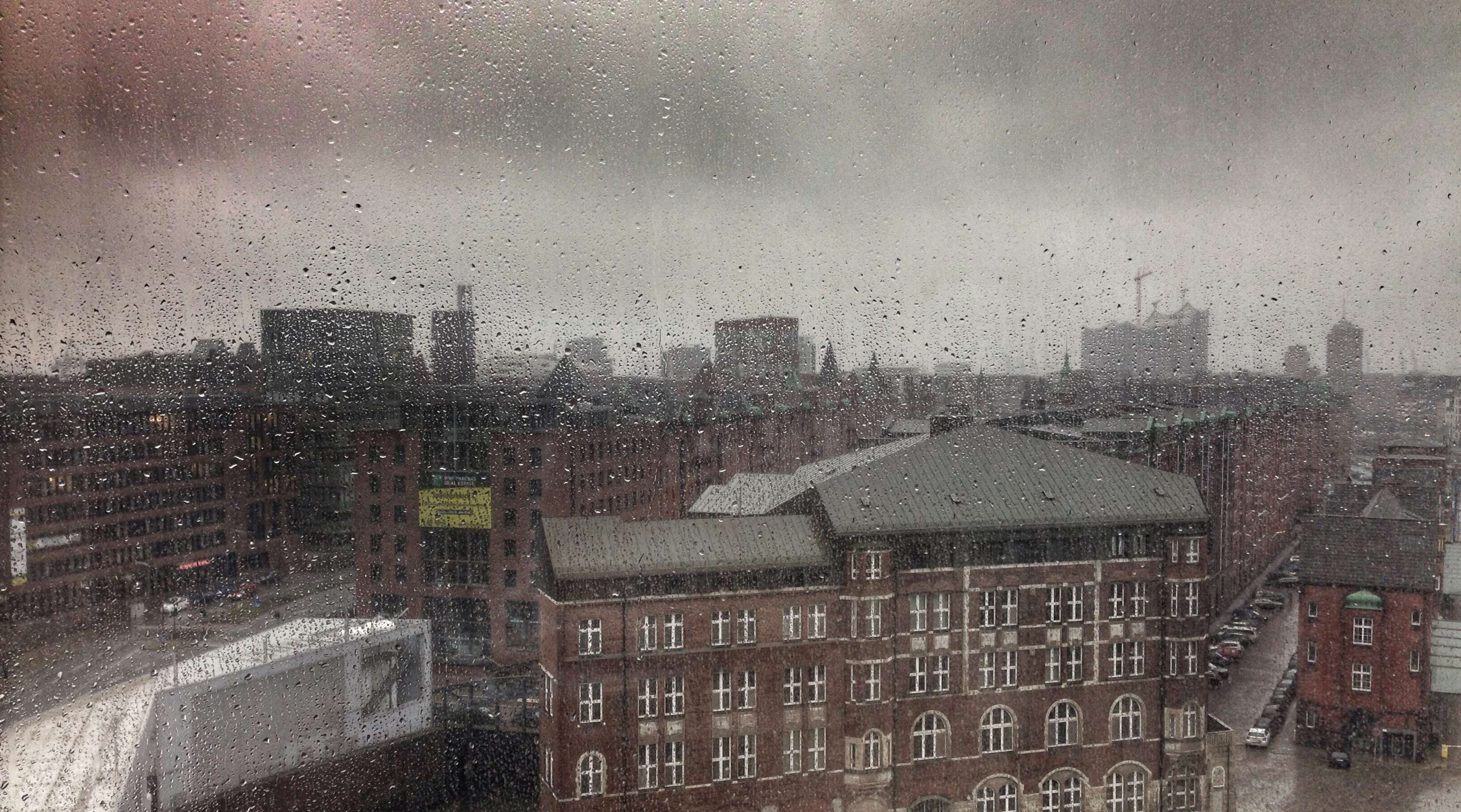 Allianz - Wohngebäudeversicherung -  Ratgeber Starkregen: Frau sitzt am Fenster und schaut dem Regen zu