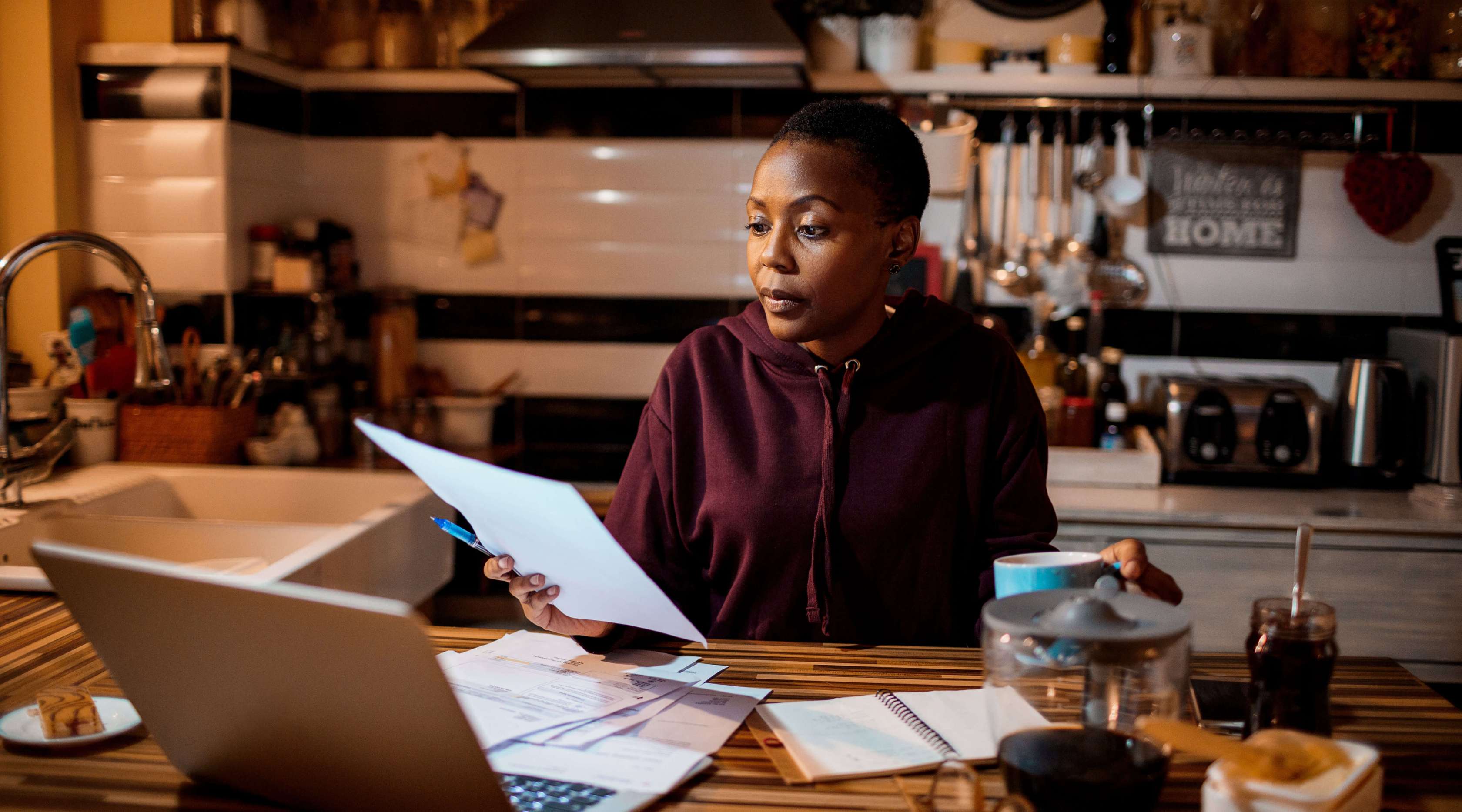 Eine Frau mit einem burgundroten Hoodie bekleidet, sitzt am Küchentisch und schaut sich ein Dokument an