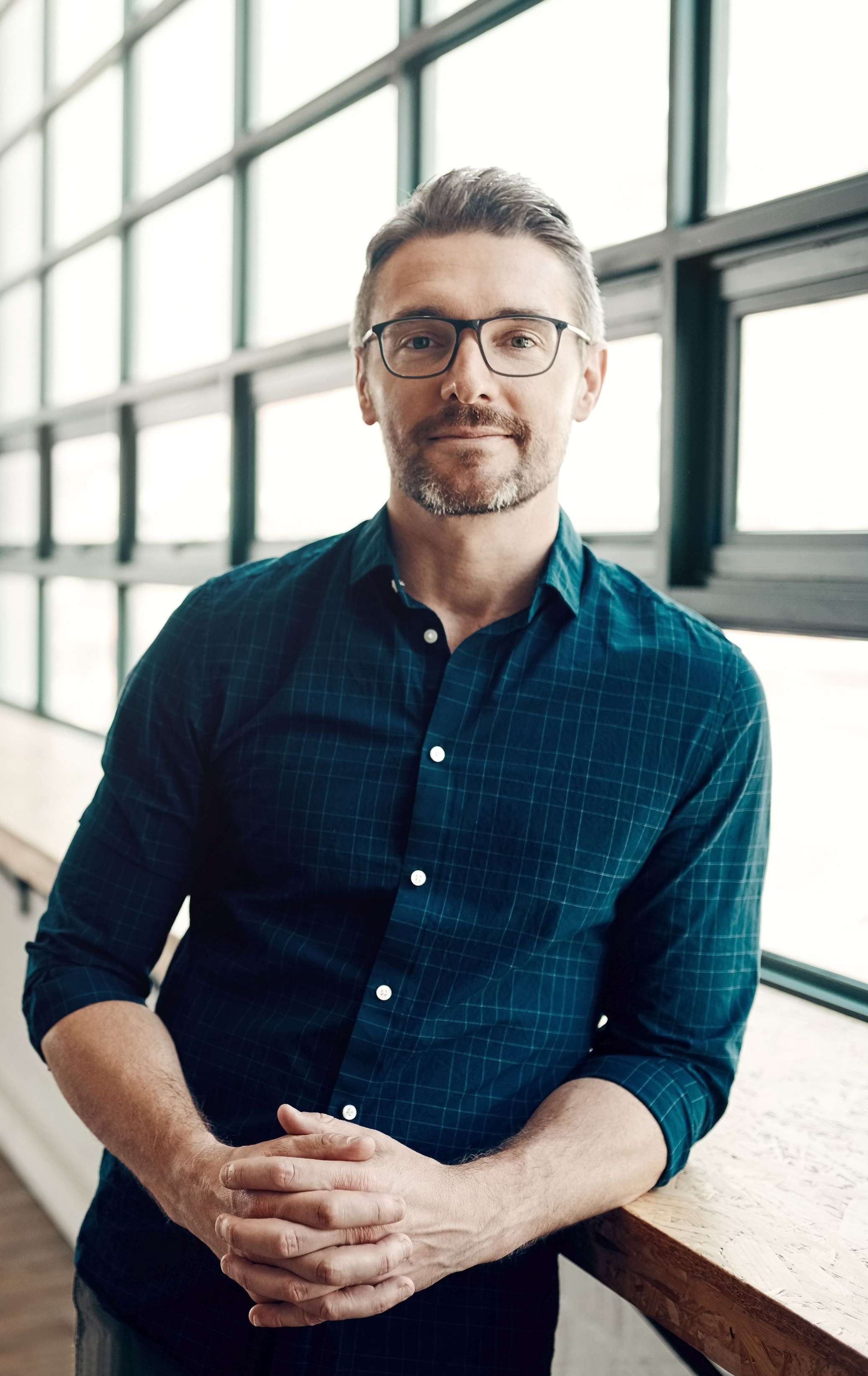 Ein bärtiger Mann mit Brille und blauem Hemd sitzt in einem Büro und schaut in die Kamera