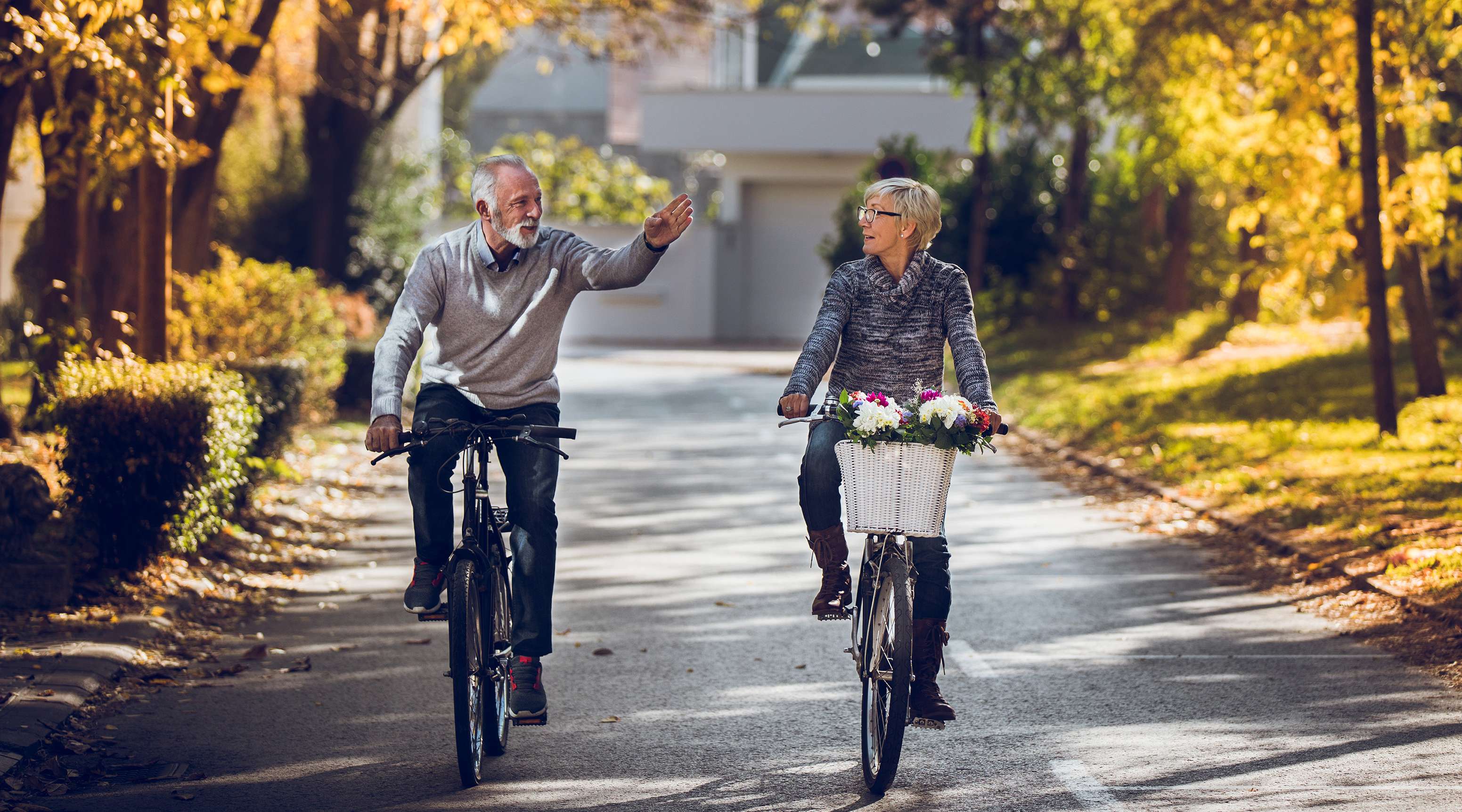 Allianz - Unfallversicherung - Fahrradkollision: ein älteres Paar auf Fahrrädern fährt eine herbstliche Straße entlang