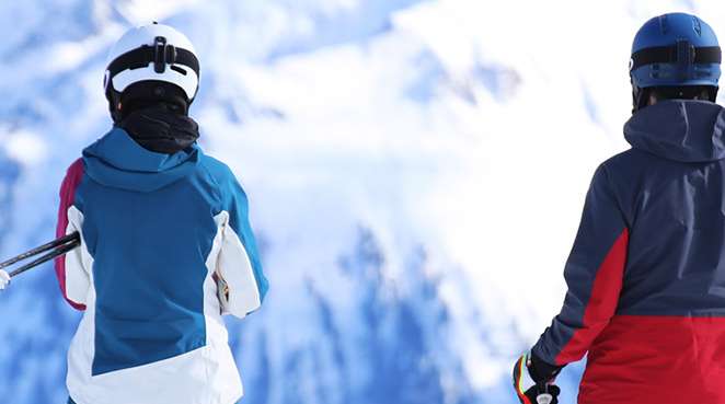 Zwei Skifahrer stehen auf einem Gipfel und schauen sich die Bergszenerie an