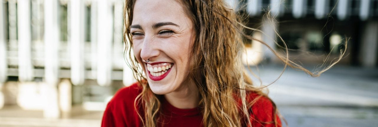 Lachende junge Frau mit rotem Shirt und rotem Lippenstift.