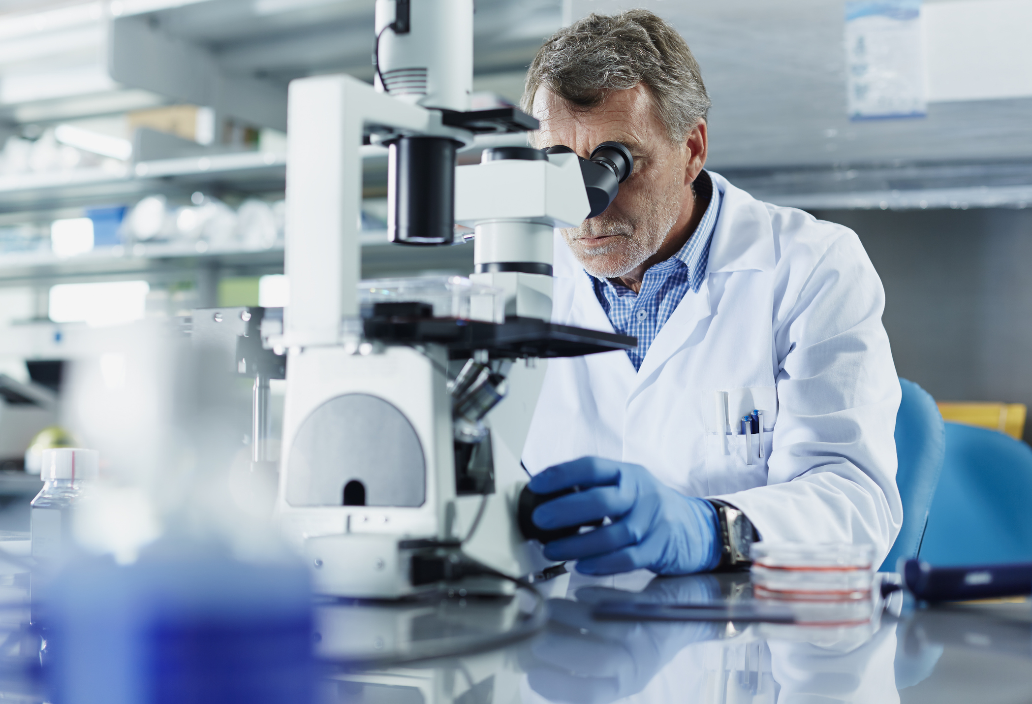 Mann in weißem Arztkittel sitzt in Labor am Mikroskop