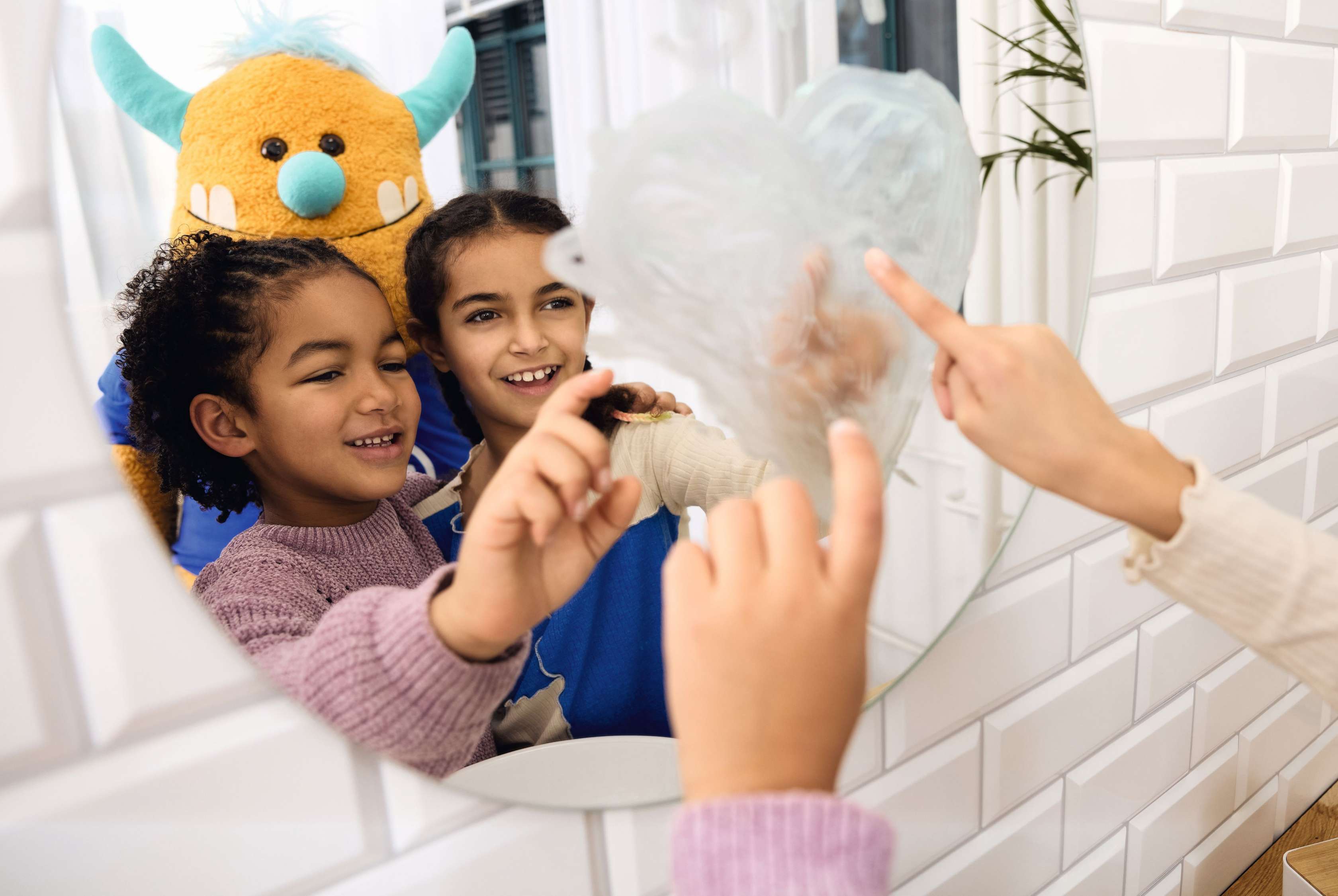 Allianz Kranken­zusatz­versicherungen für Kinder und Jugend­liche: Lachend Kinder stehen mit Kuscheltier im Badezimmer.