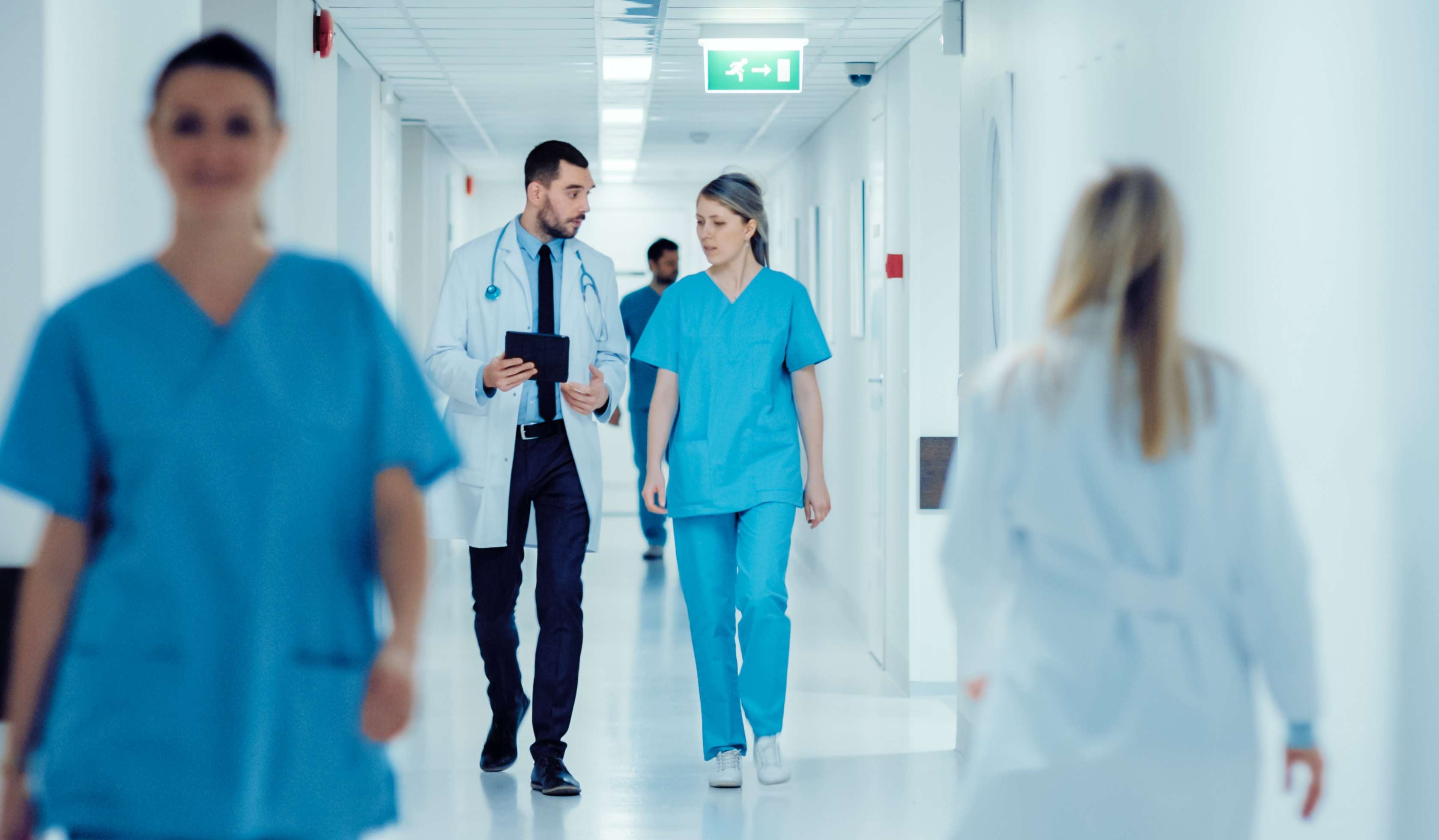 Man sieht Pfleger und Ärztinnen über einen Krankenhausflur gehen.