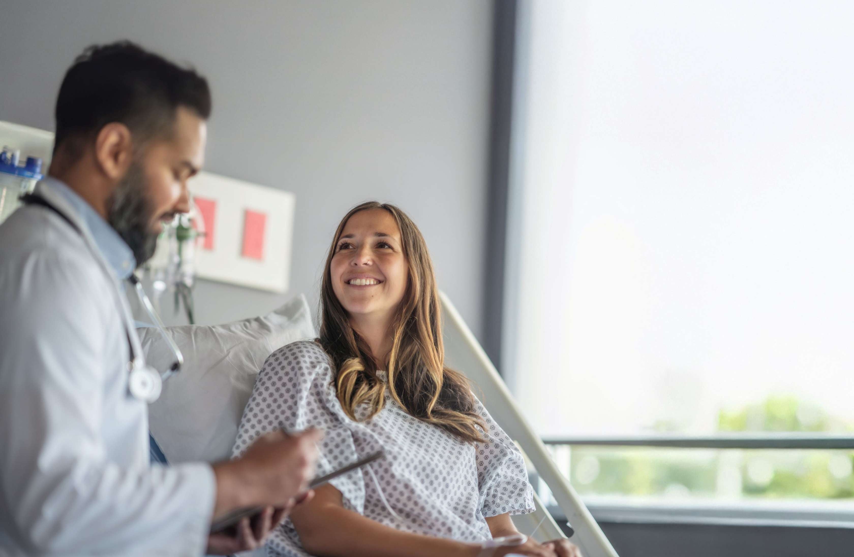Eine Patientin im Krankenhausbett schaut zu ihrem Arzt.