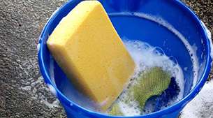 Allianz - Pferdepflege: Ein gelber Schwamm in einem blauen Eimer, gefüllt mit Spülwasser zum Putzen des Pferdes