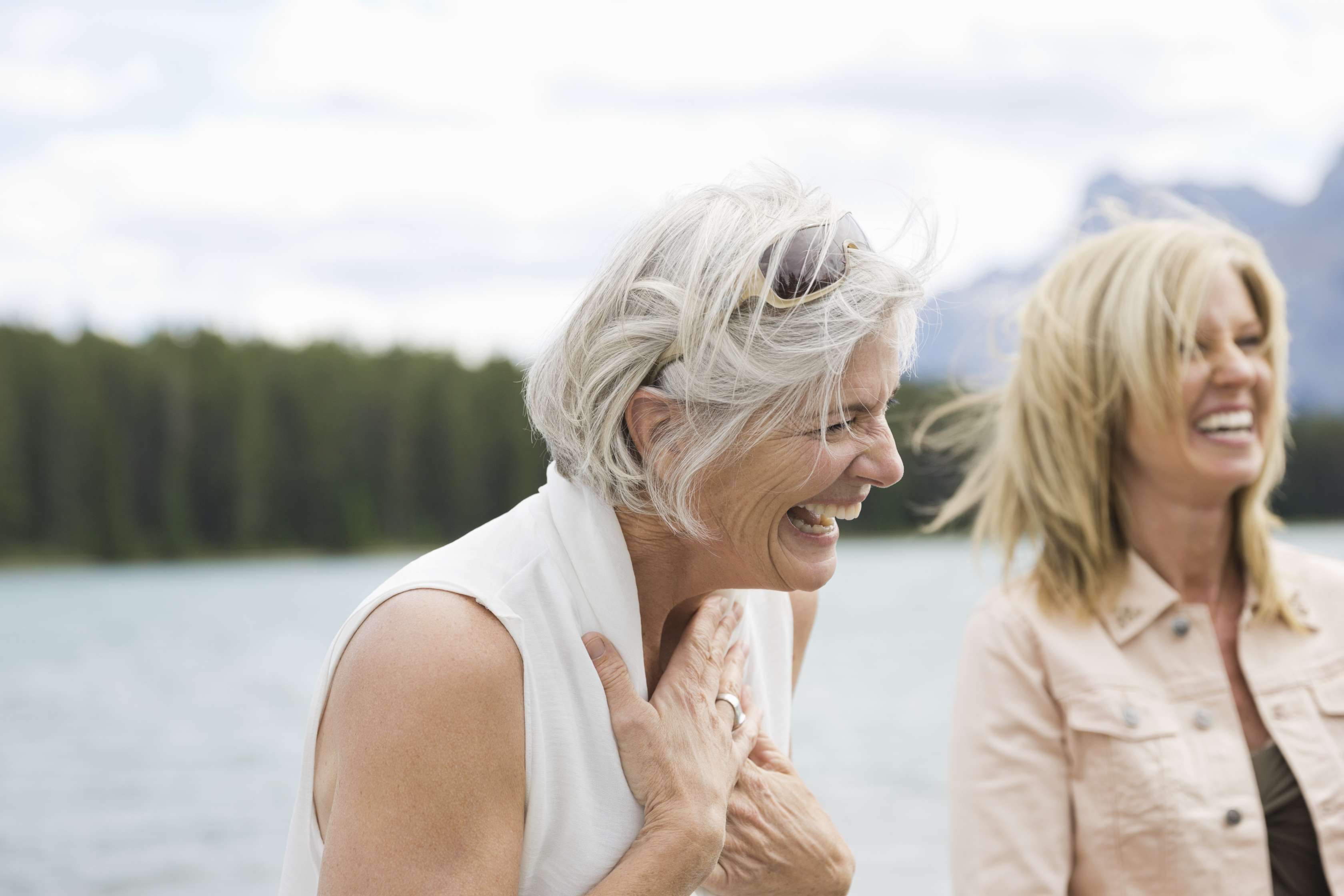 Zwei Frauen stehen gemeinsam an einem See und lachen aus tiefstem Herzen.
