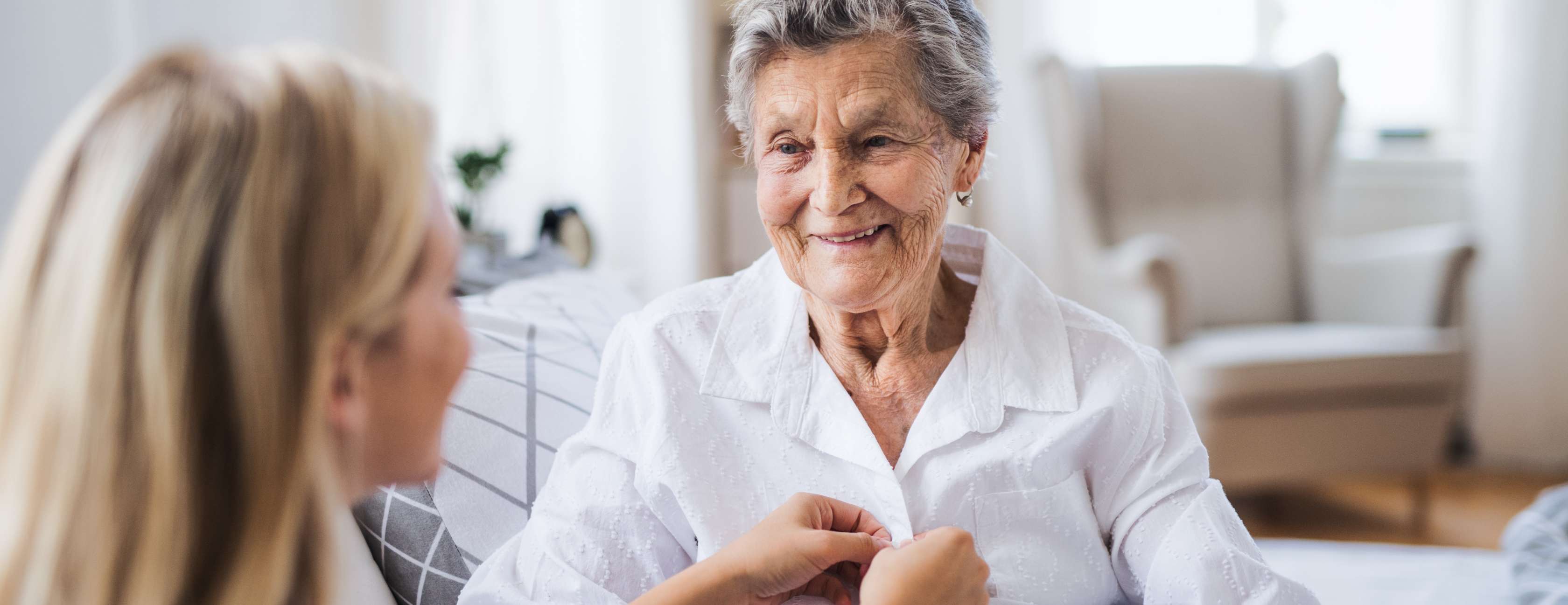 Hände einer Pflegerin umfassen Hand einer älteren Dame, die sich auf Gehstock stützt.