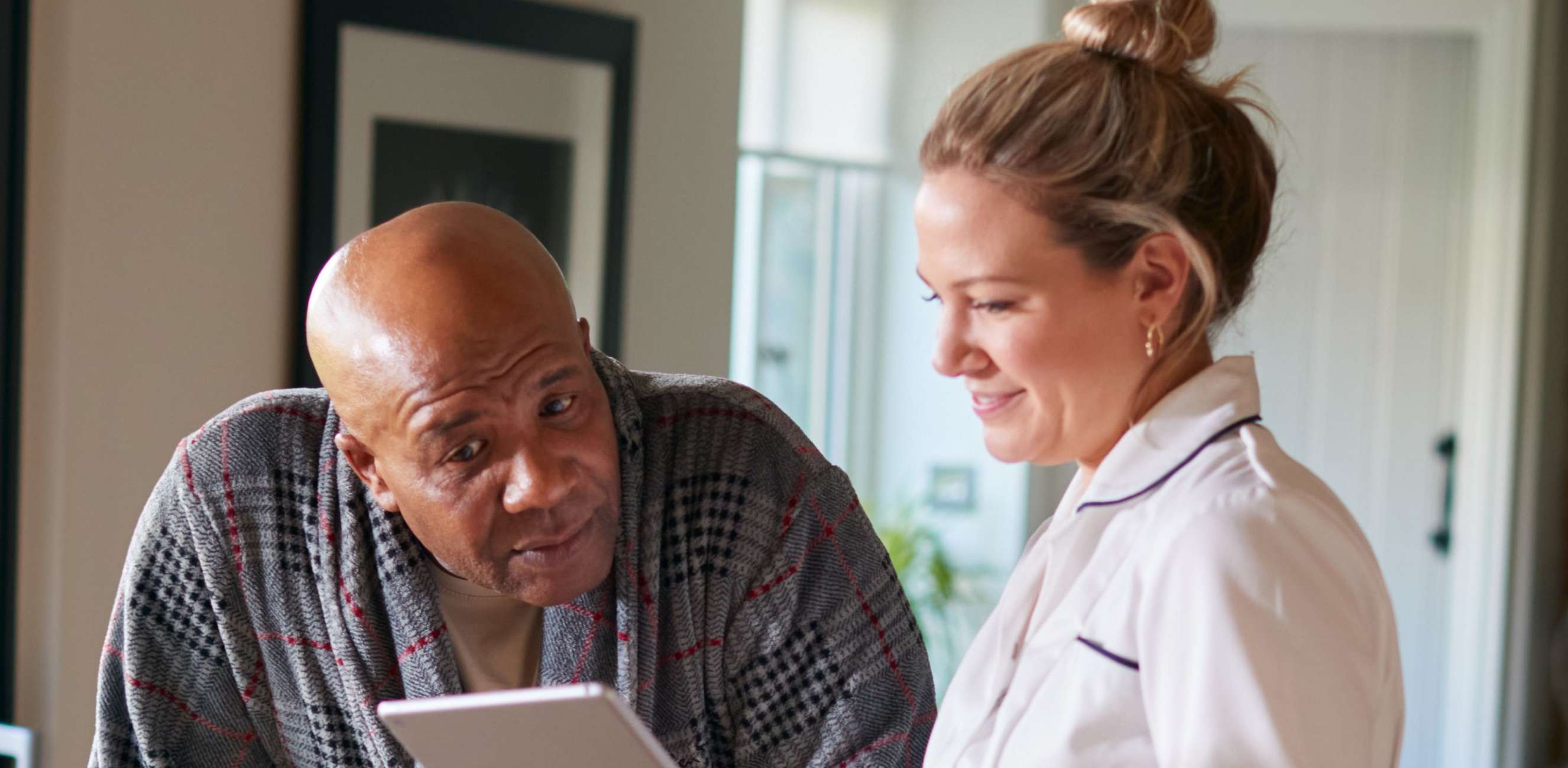Pflegetagegeldversicherung zur finanziellen Absicherung im Pflegefall: Pflegerin zeigt Mann mit Rolator etwas auf dem Tablet.