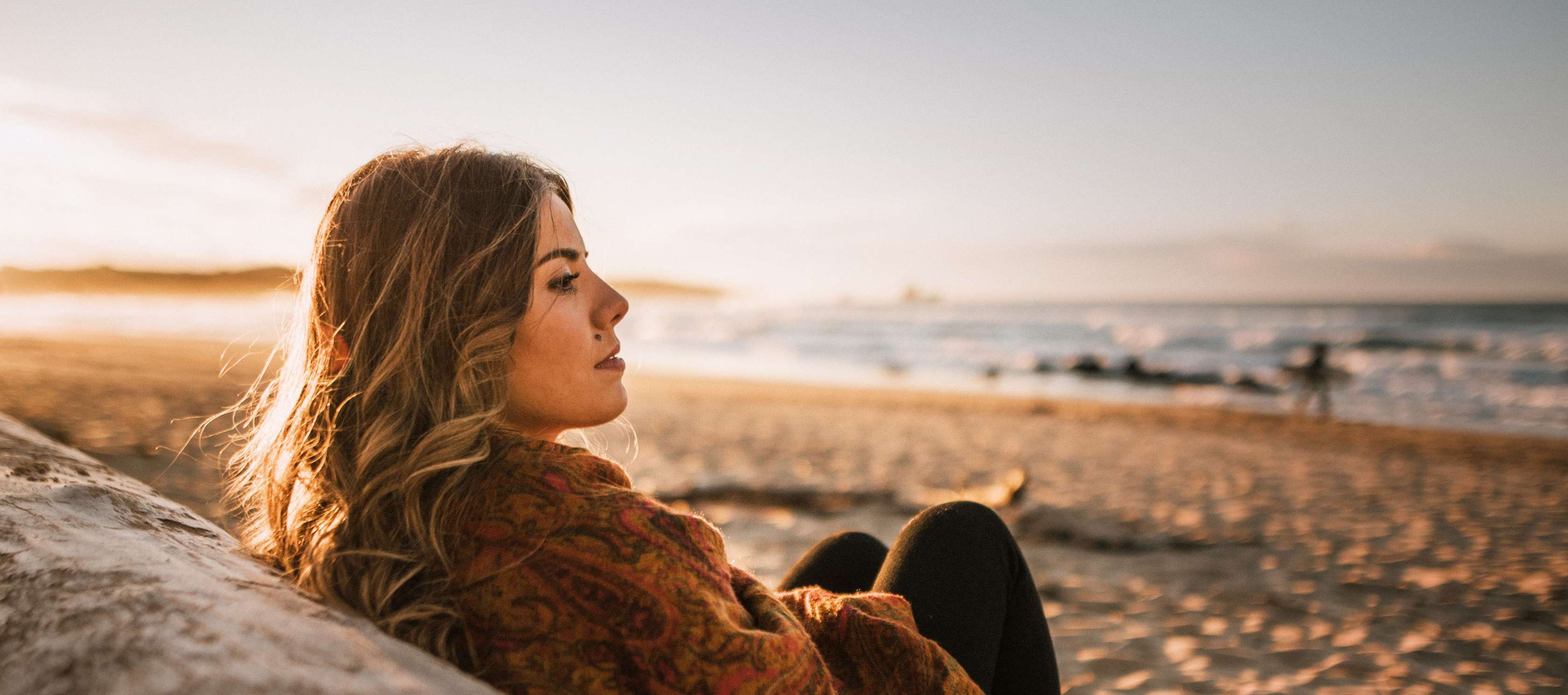 Junge Frau sitzt am Strand und schaut zum Meer