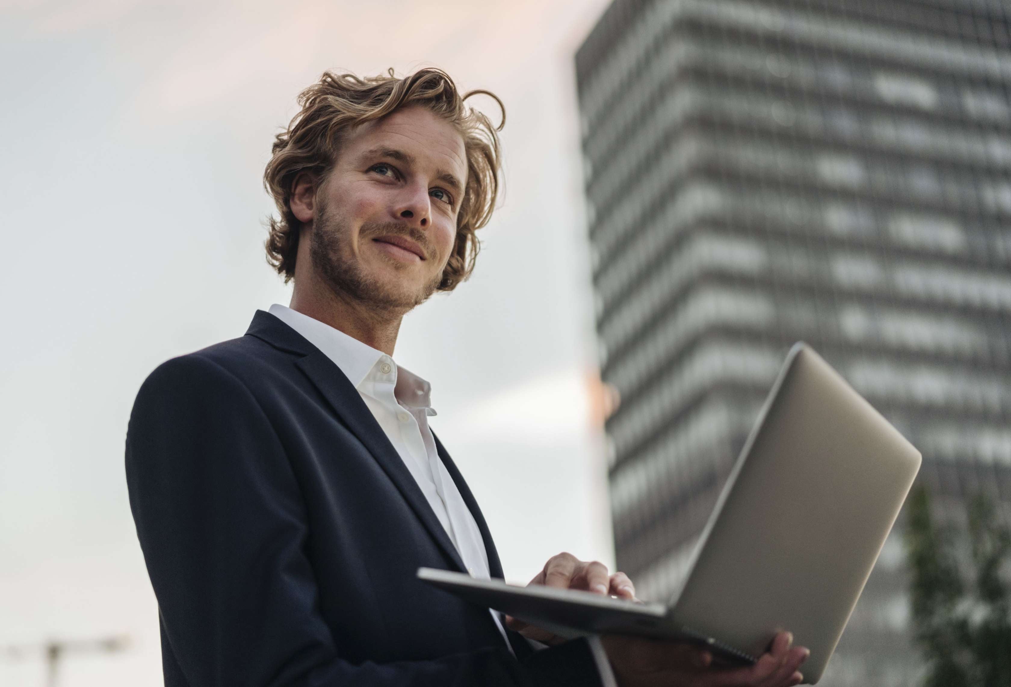 Allianz Basistarif in der Privaten Krankenversicherung: Wissenswertes im Überblick. Ein Mann steht vor einem Hochhaus und blickt in die Ferne.