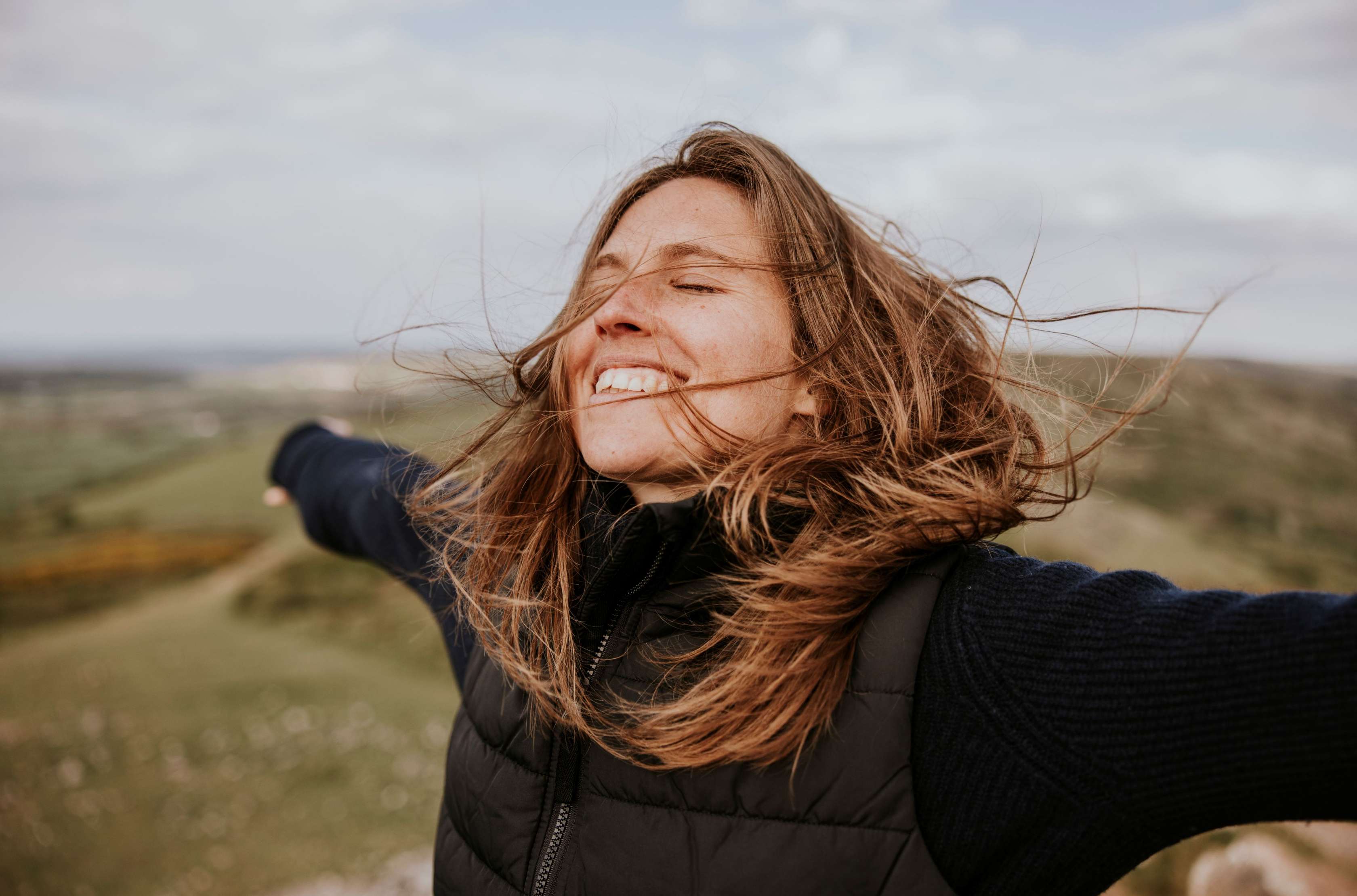 Beitragsentlastung in der PKV: Eine junge Frau steht mit ausgebreiteten Armen und lachend auf einer Wiese