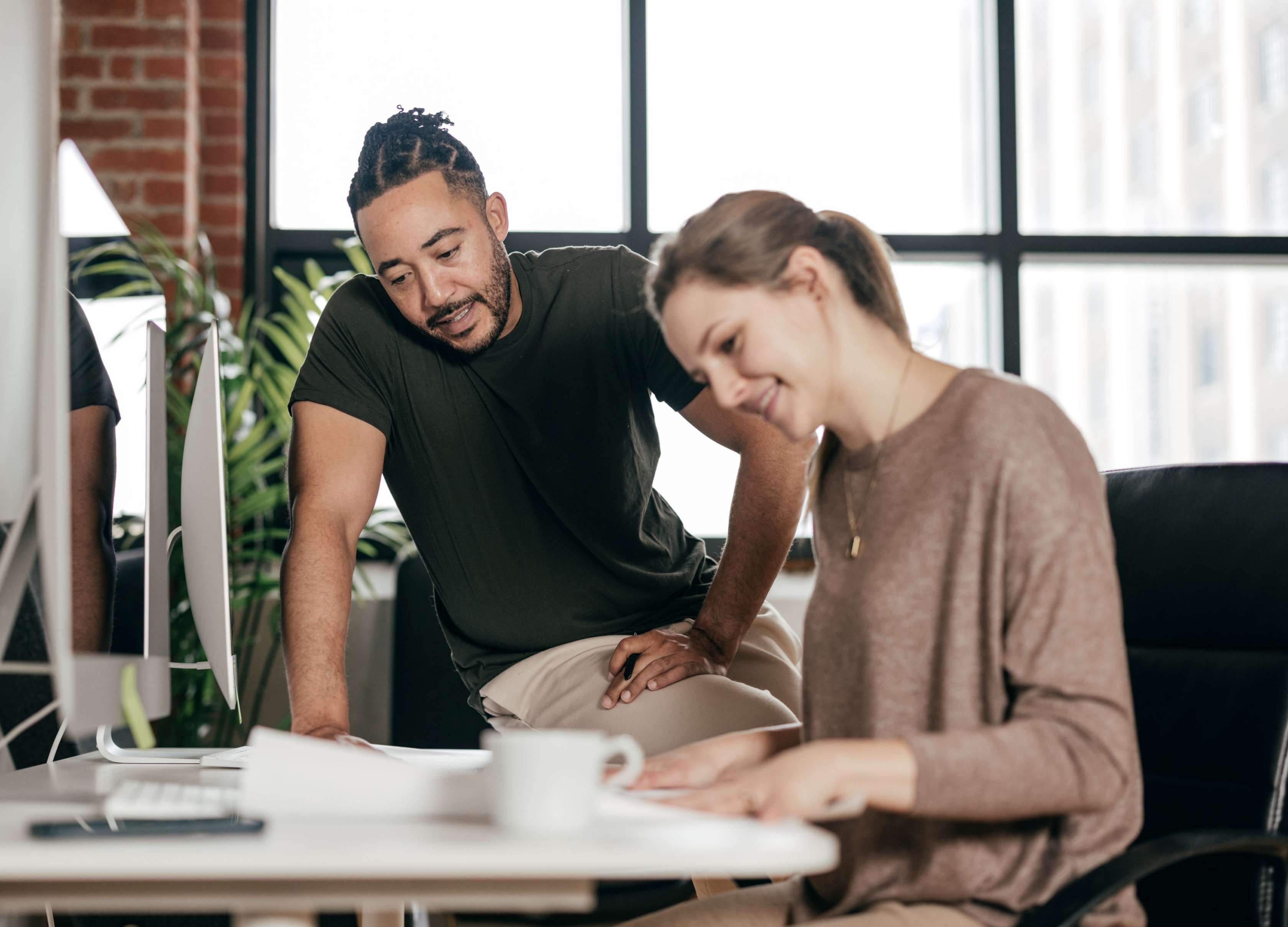 Allianz Private Kranken­versicherung: Beitrags­rück­erstattung (BRE). Ein Kollege steht bei seiner Kollegin am Schreibtisch und bespricht etwas.