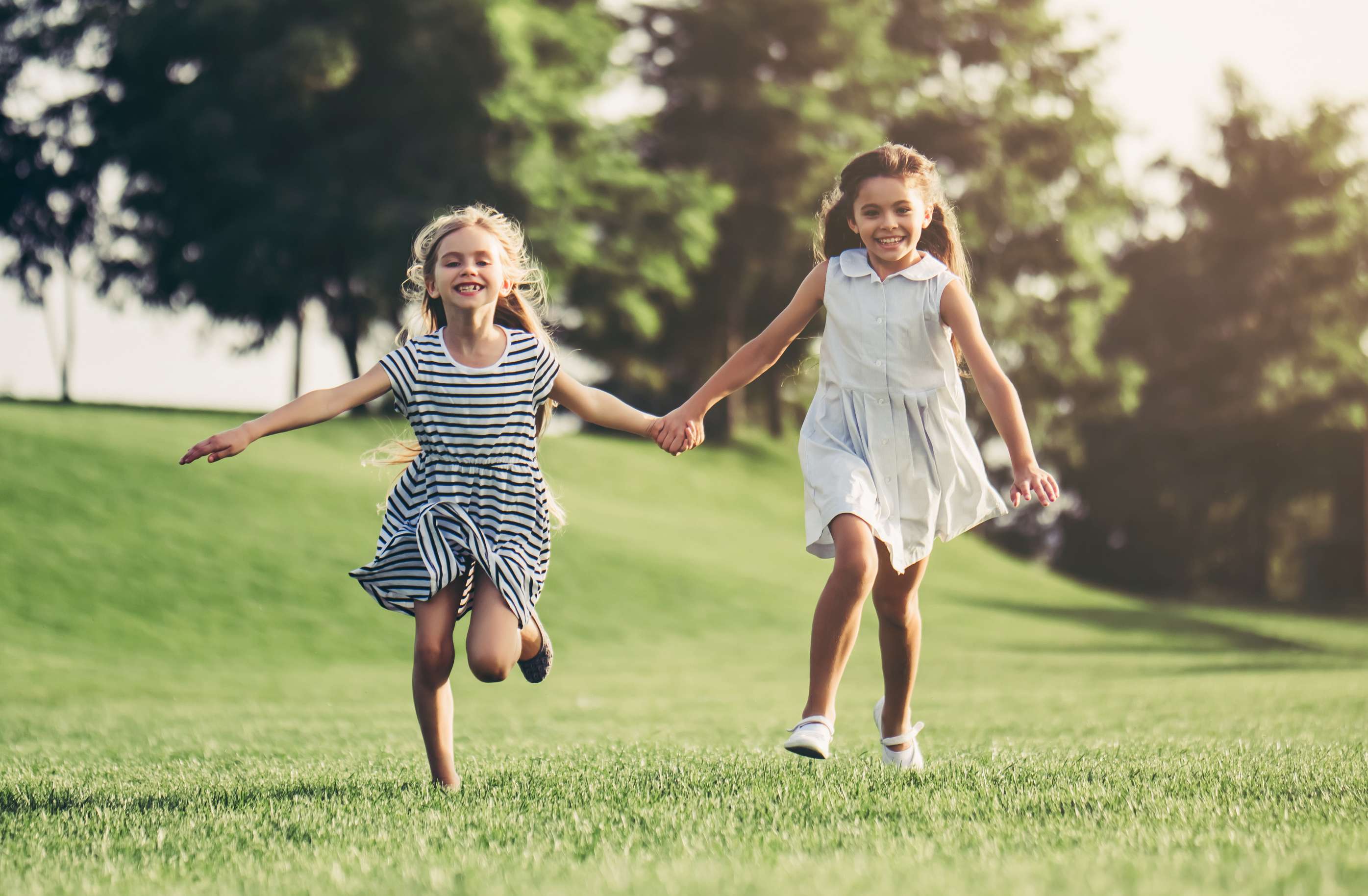 Allianz Kindergesundheit: Hausmittel und Tipps für Eltern zur Kindergesundheit. Zwei kleine Mädchen laufen händchenhaltend über eine Wiese.