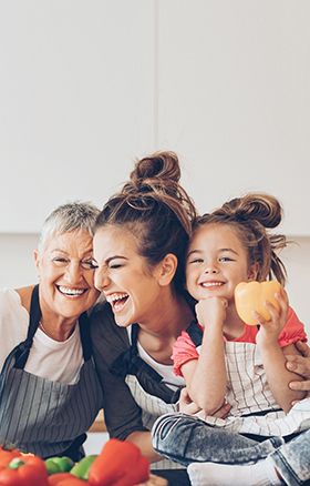 Oma, Tochter und Enkelin stehen in der Küche und kochen zusammen und lachen dabei