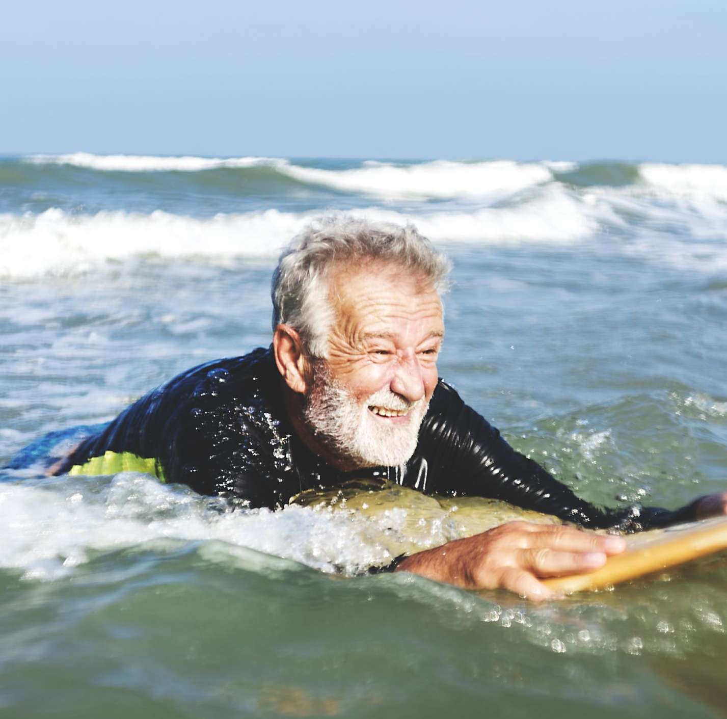 Rentner liegt im Meer auf einem Surfbrett und lernt surfen