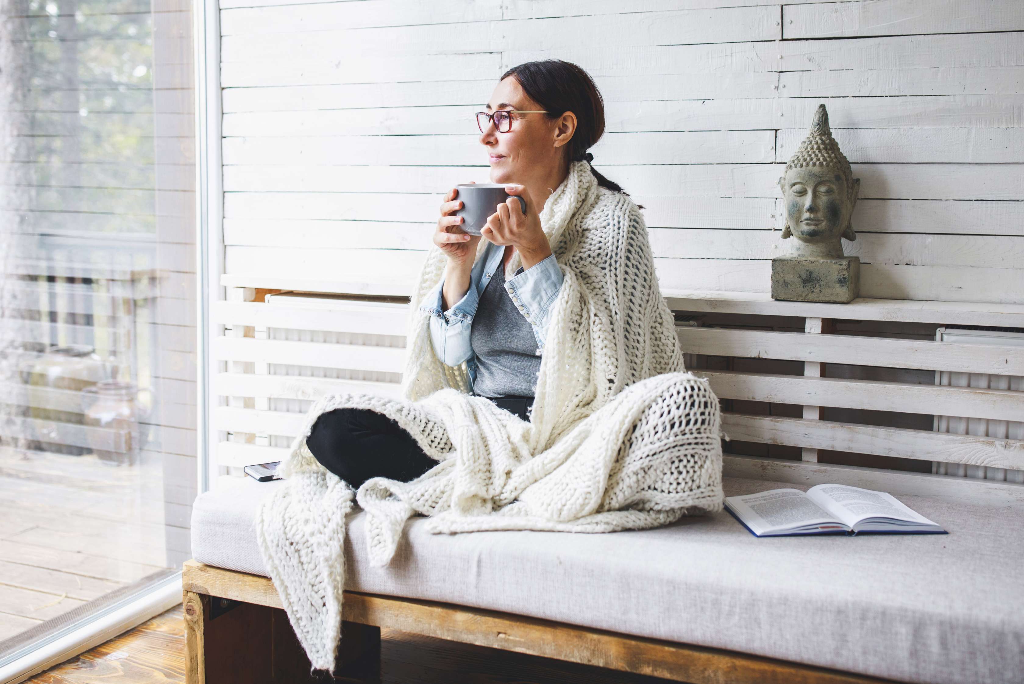 Allianz Ratgeber zur Privaten Krankenversicherung: Frau sitzt eingewickelt in einer Decke auf einer Bank und schaut aus dem Fenster