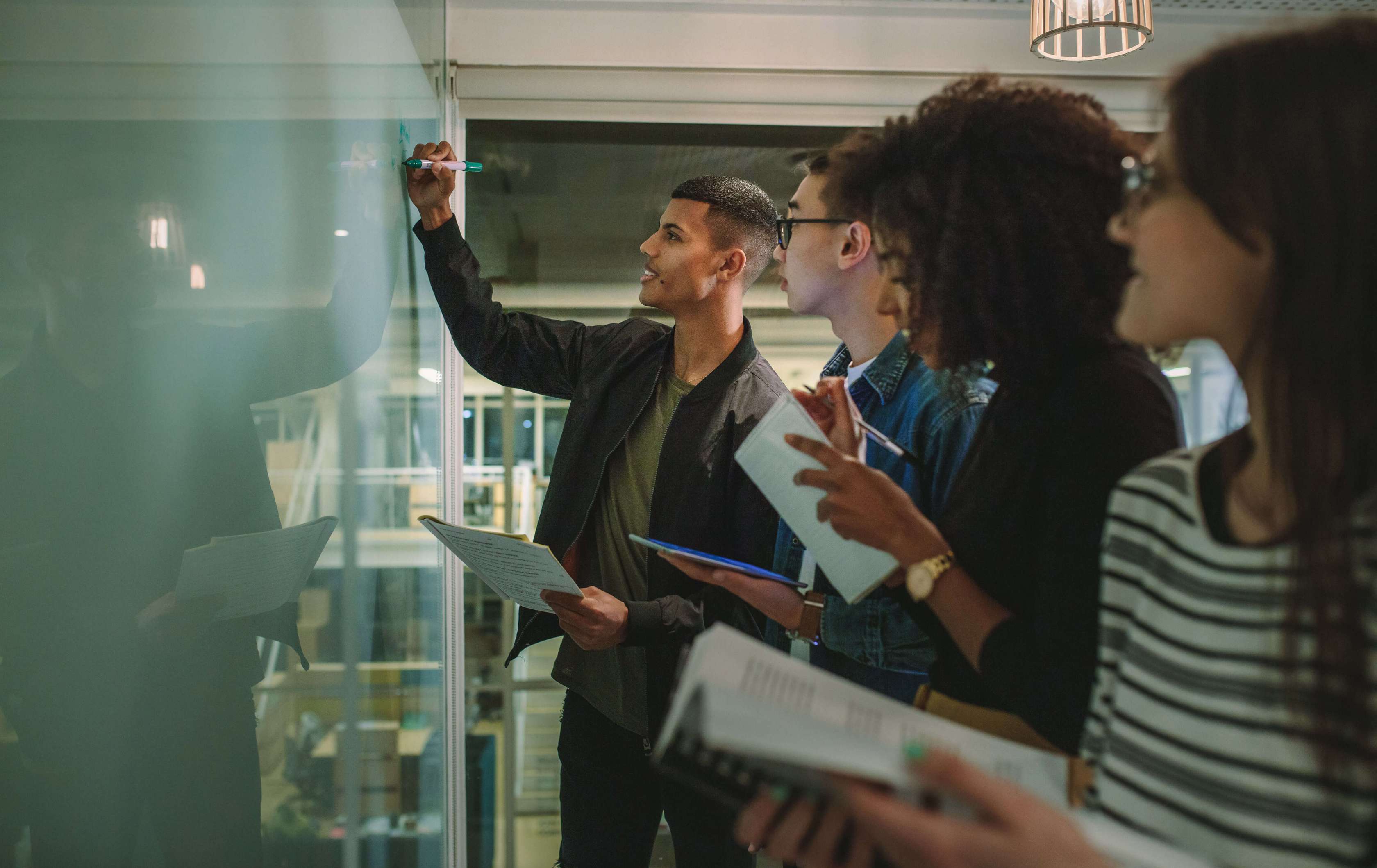 Allianz Private Krankenversicherung für das Referendariat: Ein junger Mann schreibt etwas an eine Tafel, andere Personen schauen ihm dabei zu.