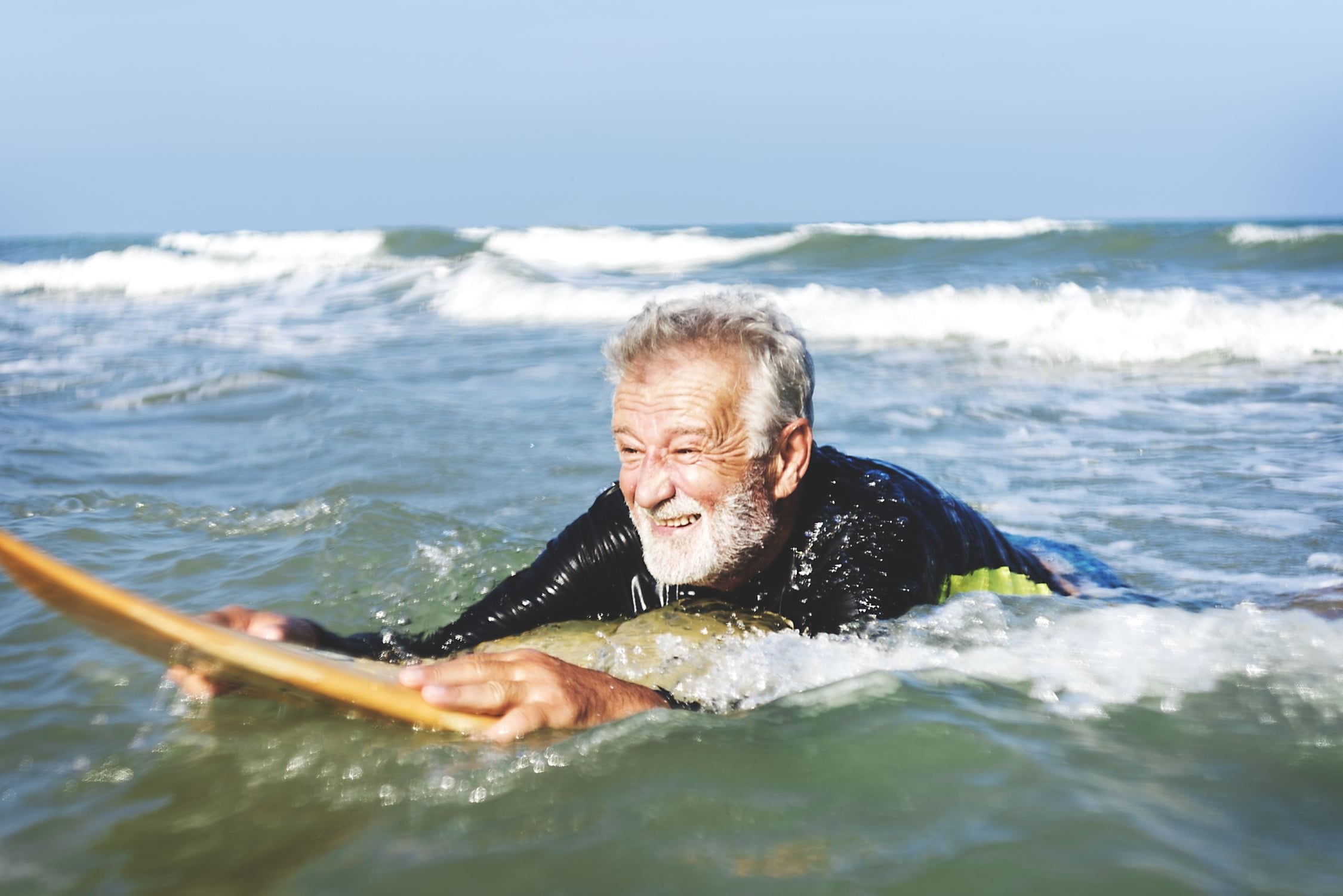 Allianz Private Krankenversicherung für Rentner: Älterer Mann schwimmt mit einem Surfbrett im Wasser