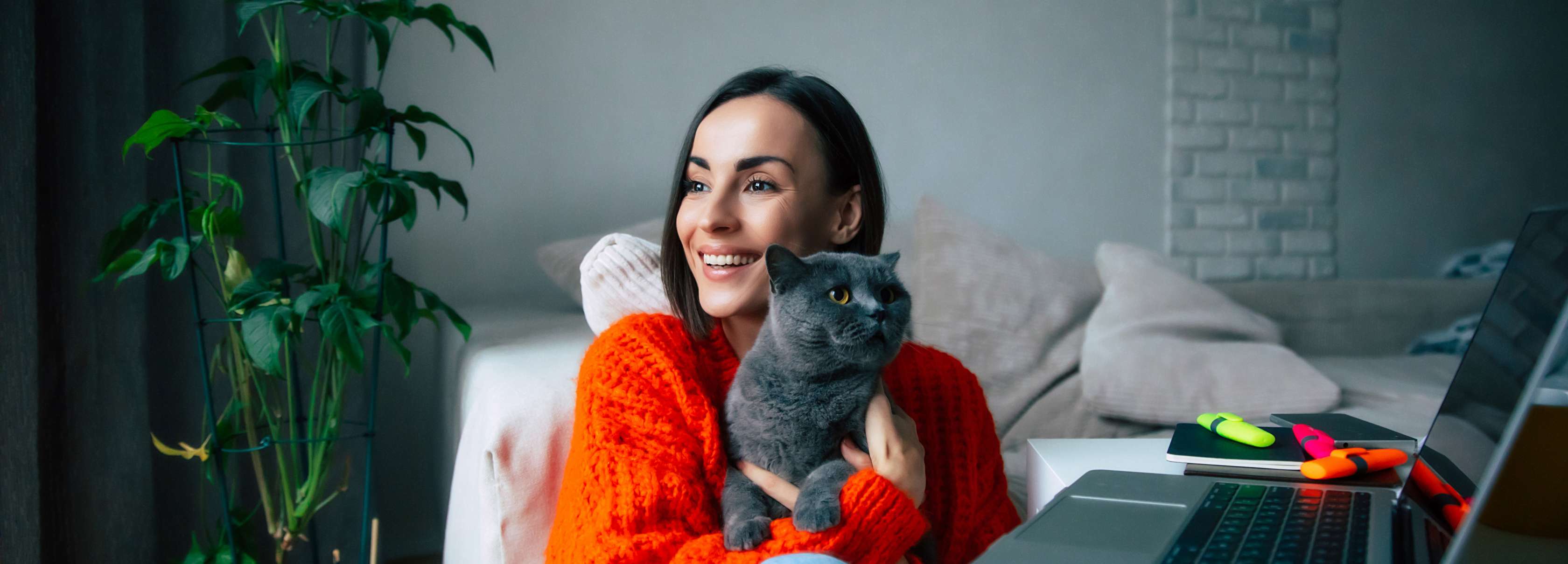 Eine Frau sitzt auf dem Fußboden vor der Couch mit einer Katze auf dem Arm