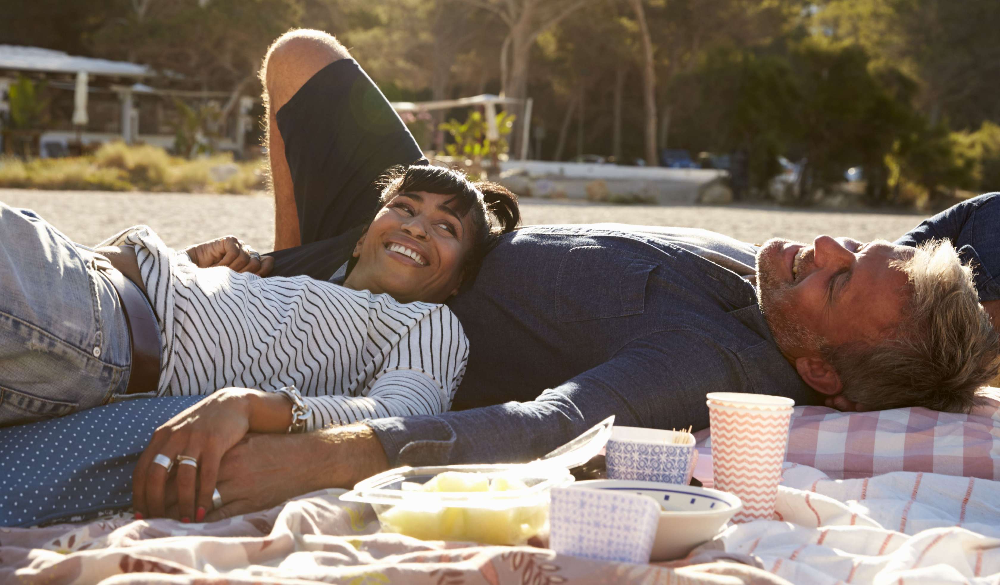 Allianz Zahnzusatzversicherung im Ausland schützt auch auf Reisen. Pärchen liegt auf einer Picknickdecke am Strand.
