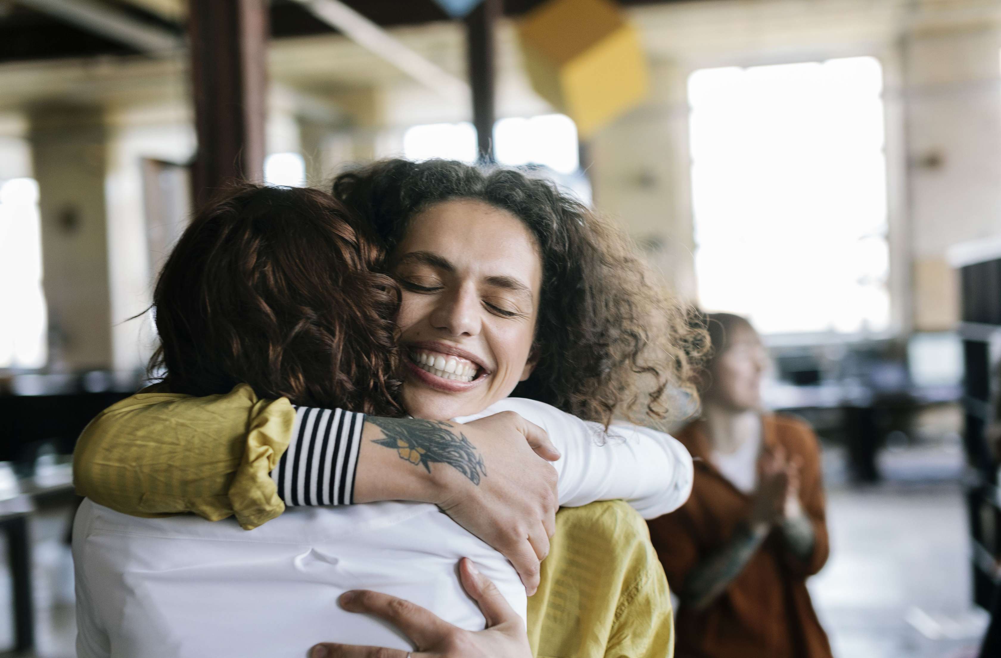 Zahnzusatzversicherung Kiefer­orthopädie für Erwachsene: Frau umarmt eine andere Frau und lächelt