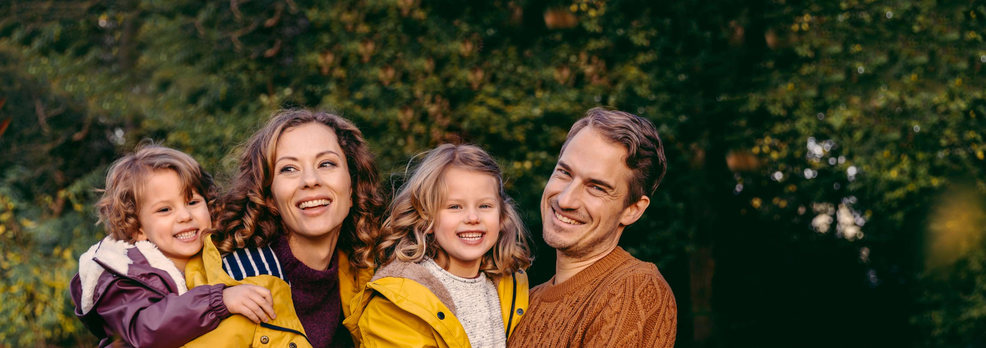 Familie mit Frau, Mann und zwei Kindern steht auf einer grünen Wiese und lächelt in die Kamera