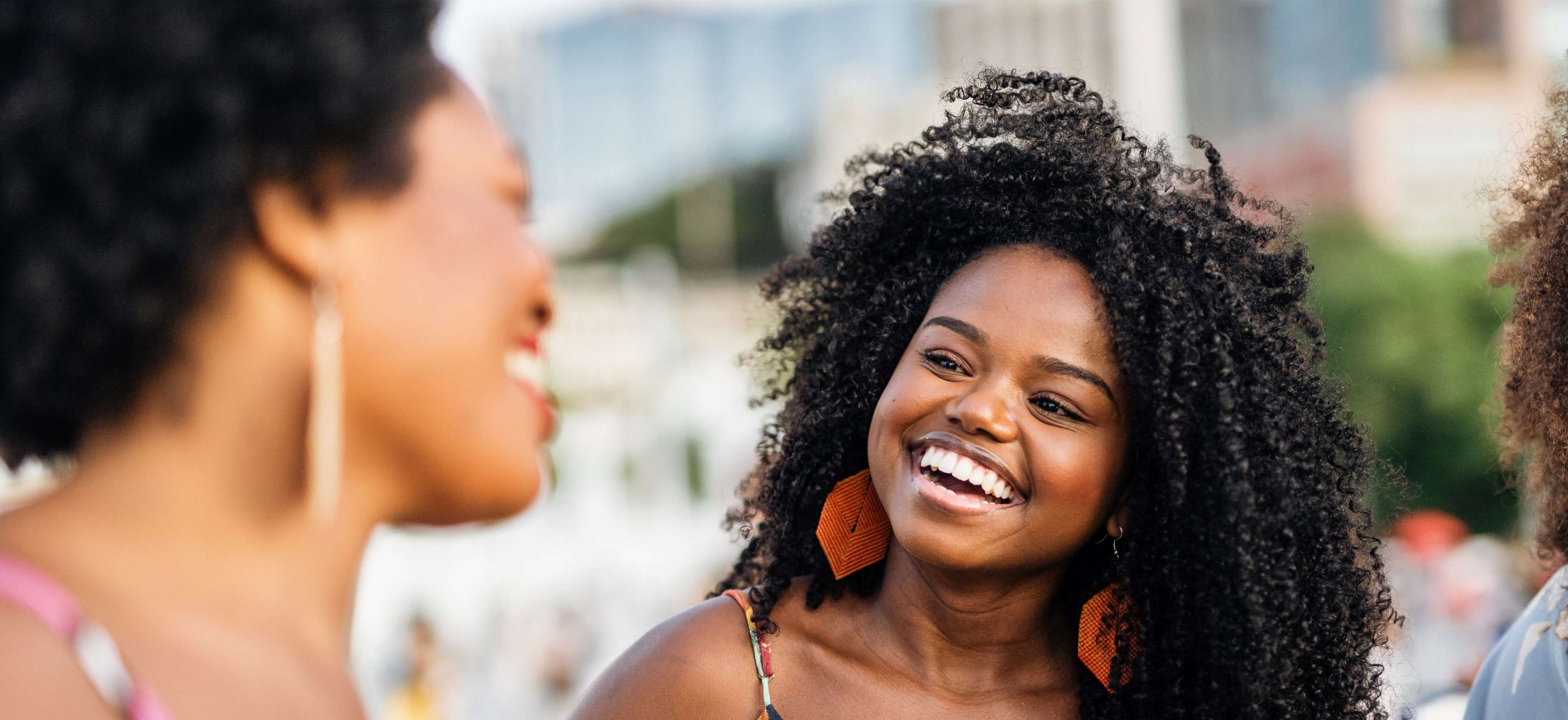 Zahnzusatzversicherung mit Sofortschutz: Zwei Frauen in bunten Sommerkleidern schauen sich an und lachen zusammen.