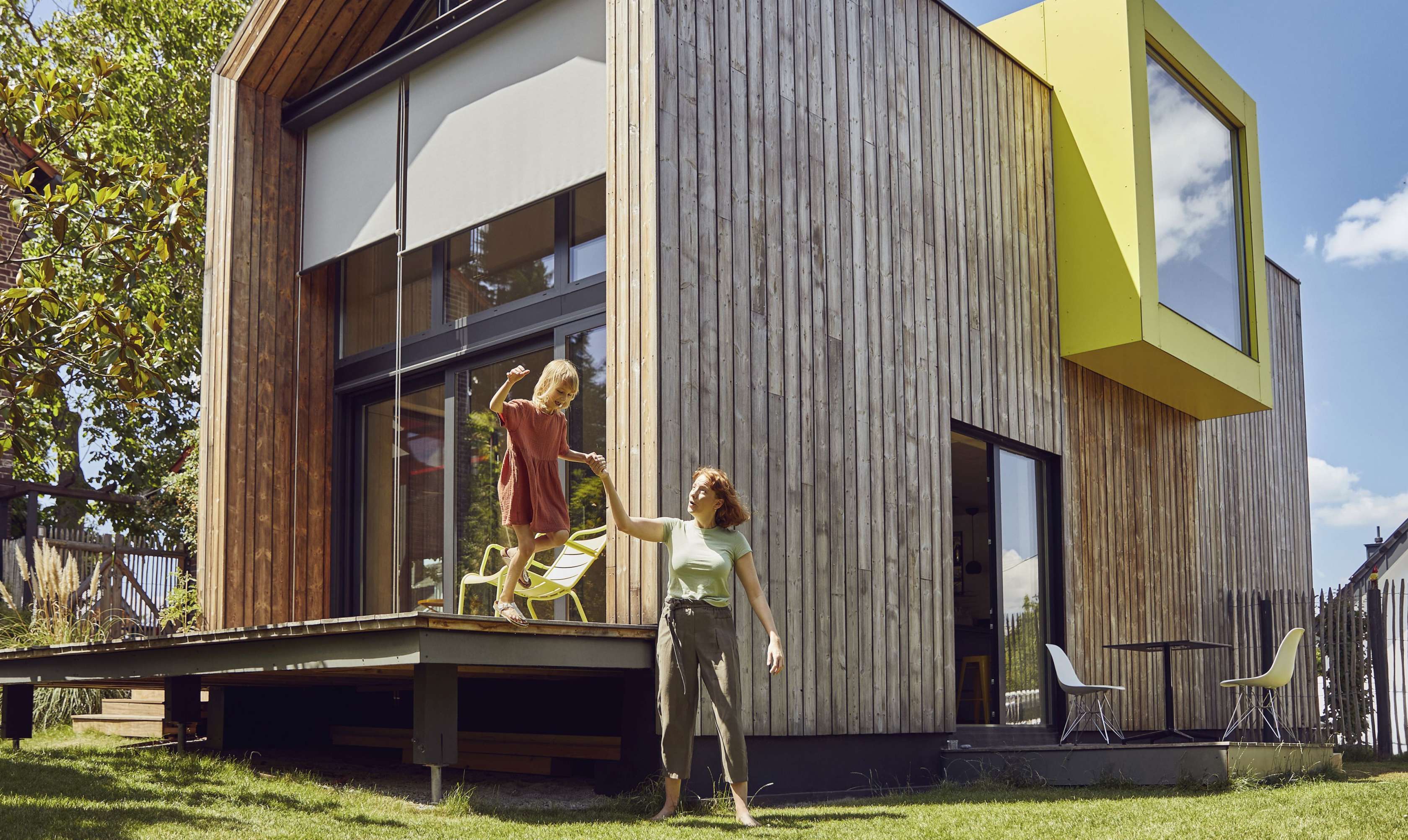 Allianz Baufinanzierung: Eine Mutter hilft ihrer Tochter bei einem Sprung von der Terrasse ihres Hauses