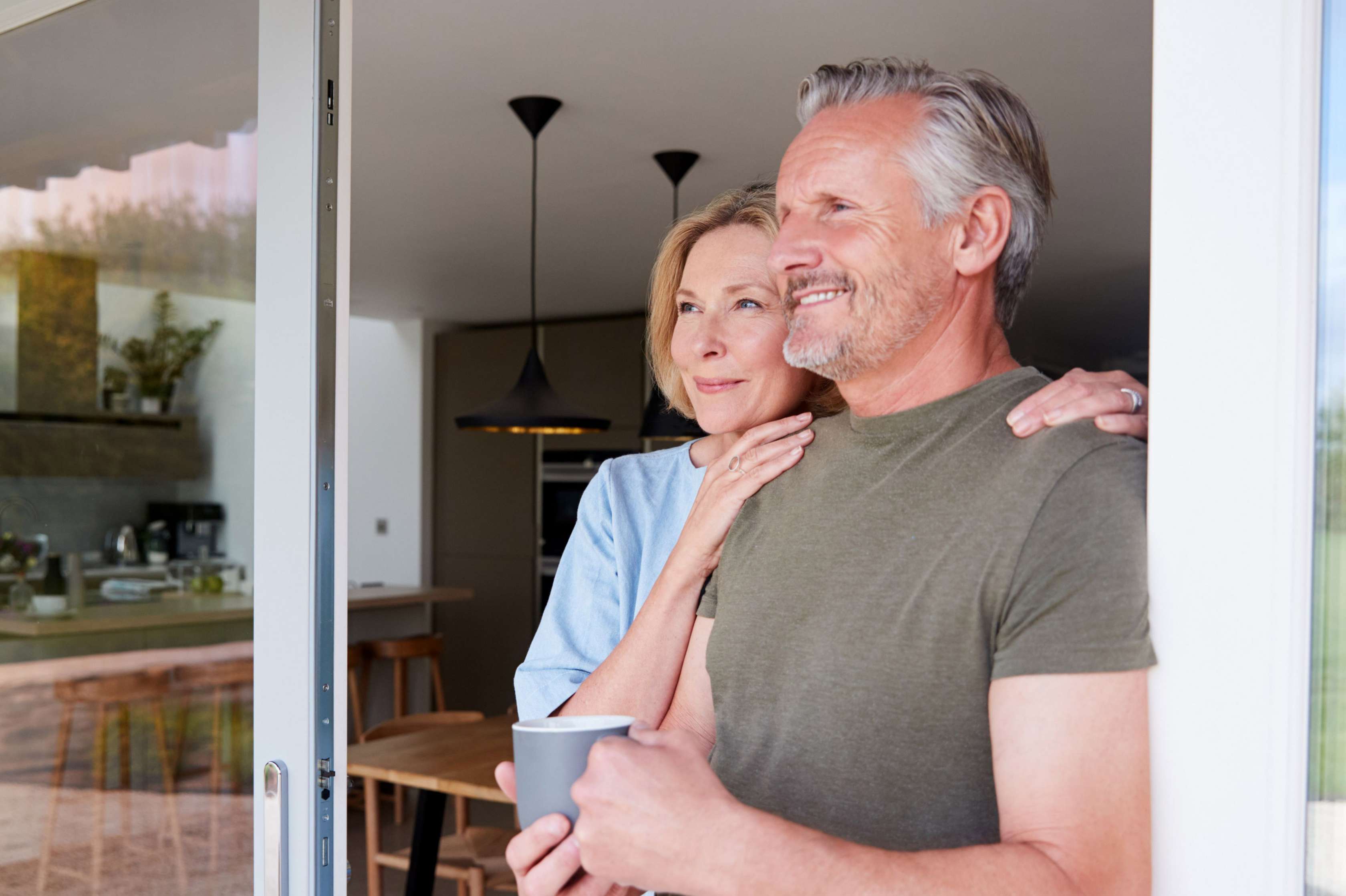 Allianz Anschlussfinanzierung - Ein lächelndes Paar steht in der Tür ihres Hauses und schaut nach draußen.