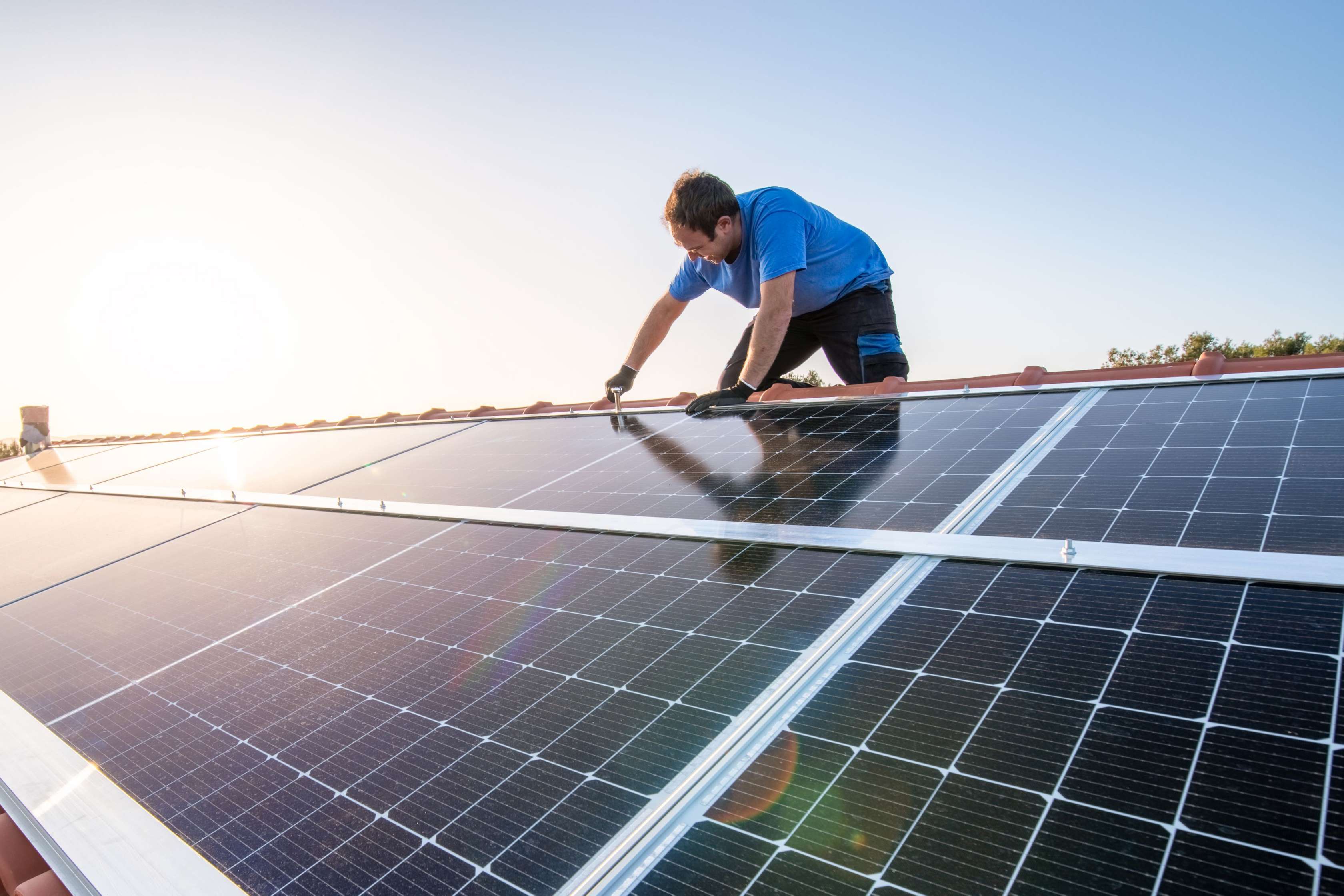 Allianz energetische Sanierung: Handwerker installiert Fotovoltaik-Anlagen auf dem Dach eines Hauses.