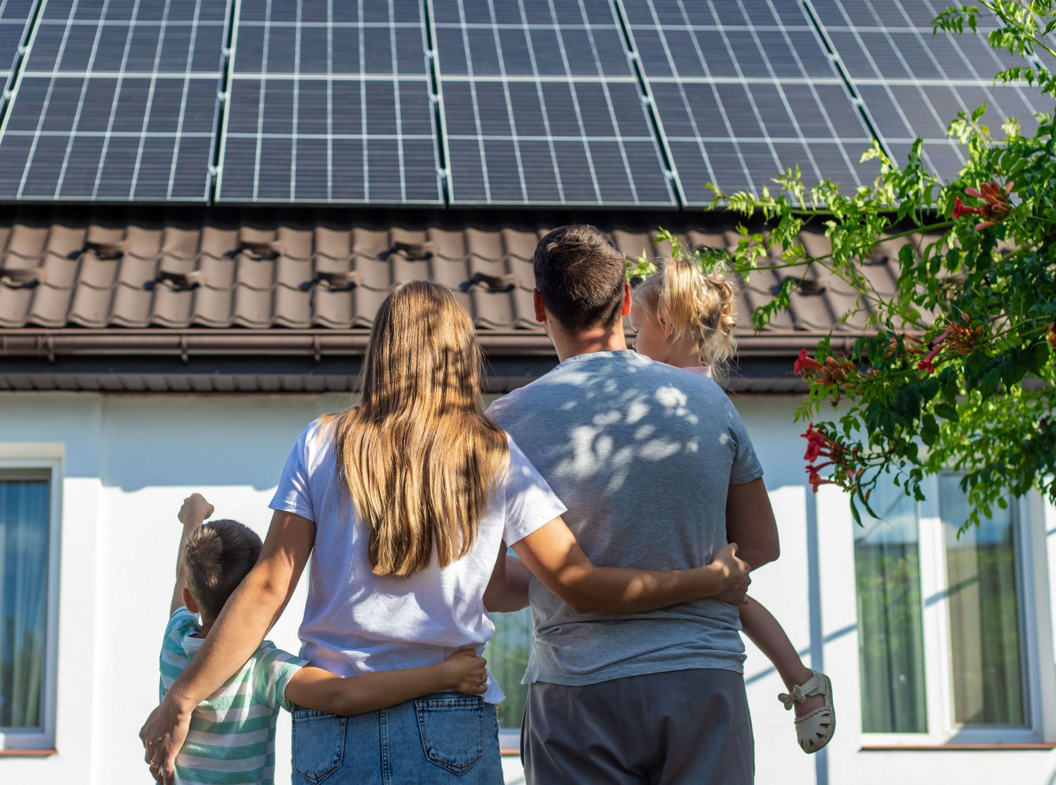 Allianz energetische Sanierung: Eine Familie mit zwei Kindern schaut auf die Fotovoltaik-Anlagen auf dem Dach ihres Hauses.