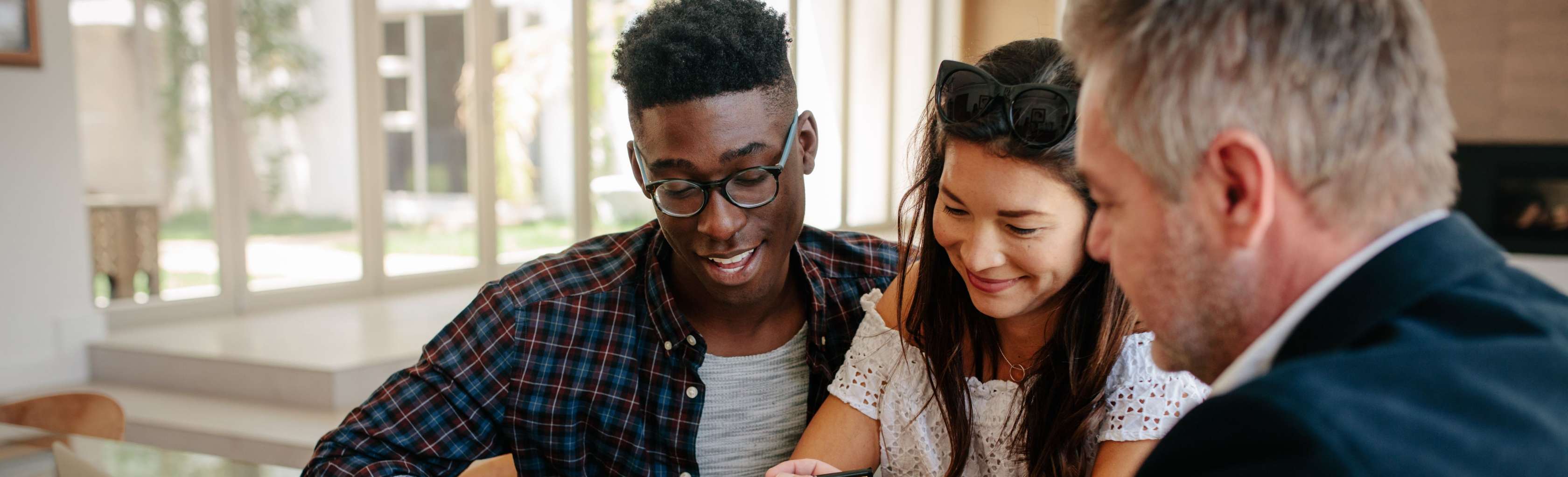 Allianz Bauzinsen: Ein Paar sitzt an einem Tisch und bespricht Dokumente mit einem Berater, der einen Laptop vor sich hat.
