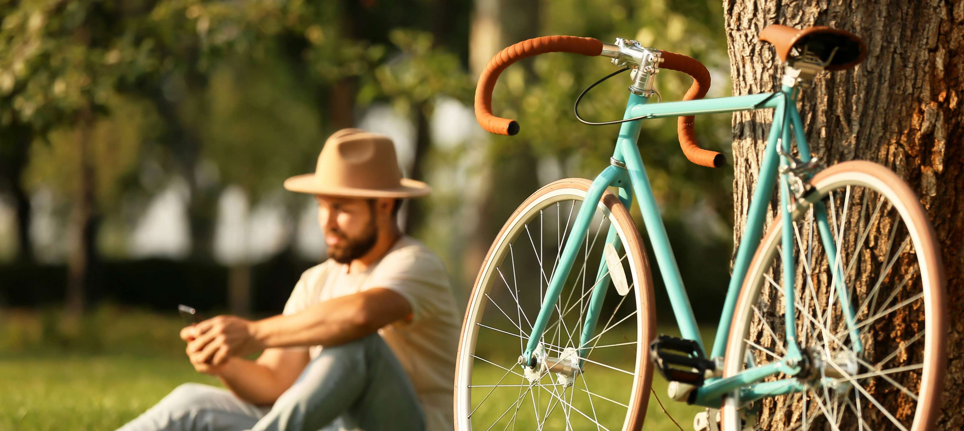Fahrrad registrieren: Mann sitzt an einem Baum und schaut auf sein Smartphone, neben ihm steht sein Fahrrad
