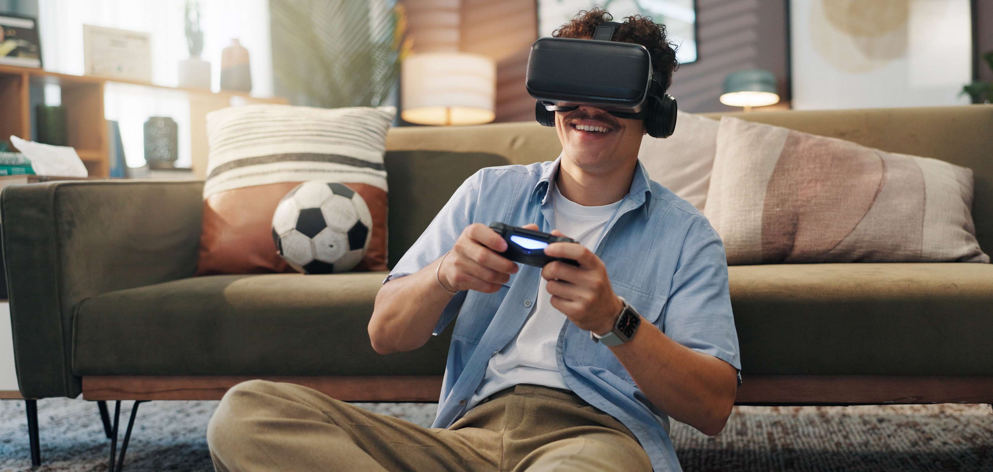 Allianz Geräteversicherung: Mann sitzt mit VR-Brille und Controller vor dem Sofa