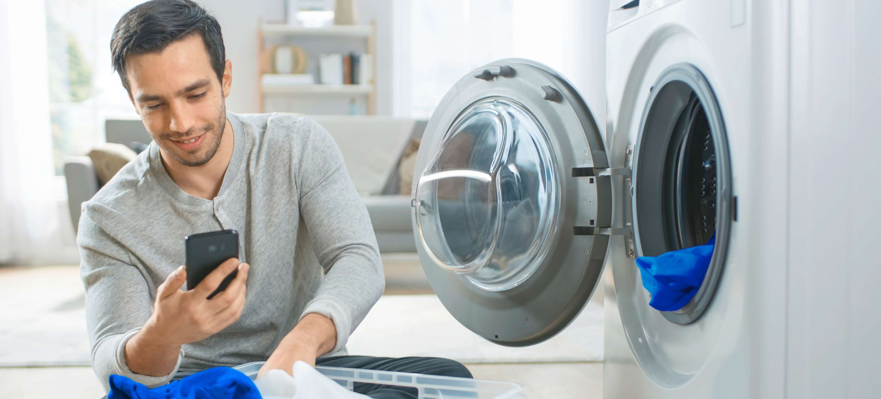 Hausrat-Haftpflicht-Kombi: Ein junger Mann sitzt mit Wäsche vor einer offenen Waschmaschine