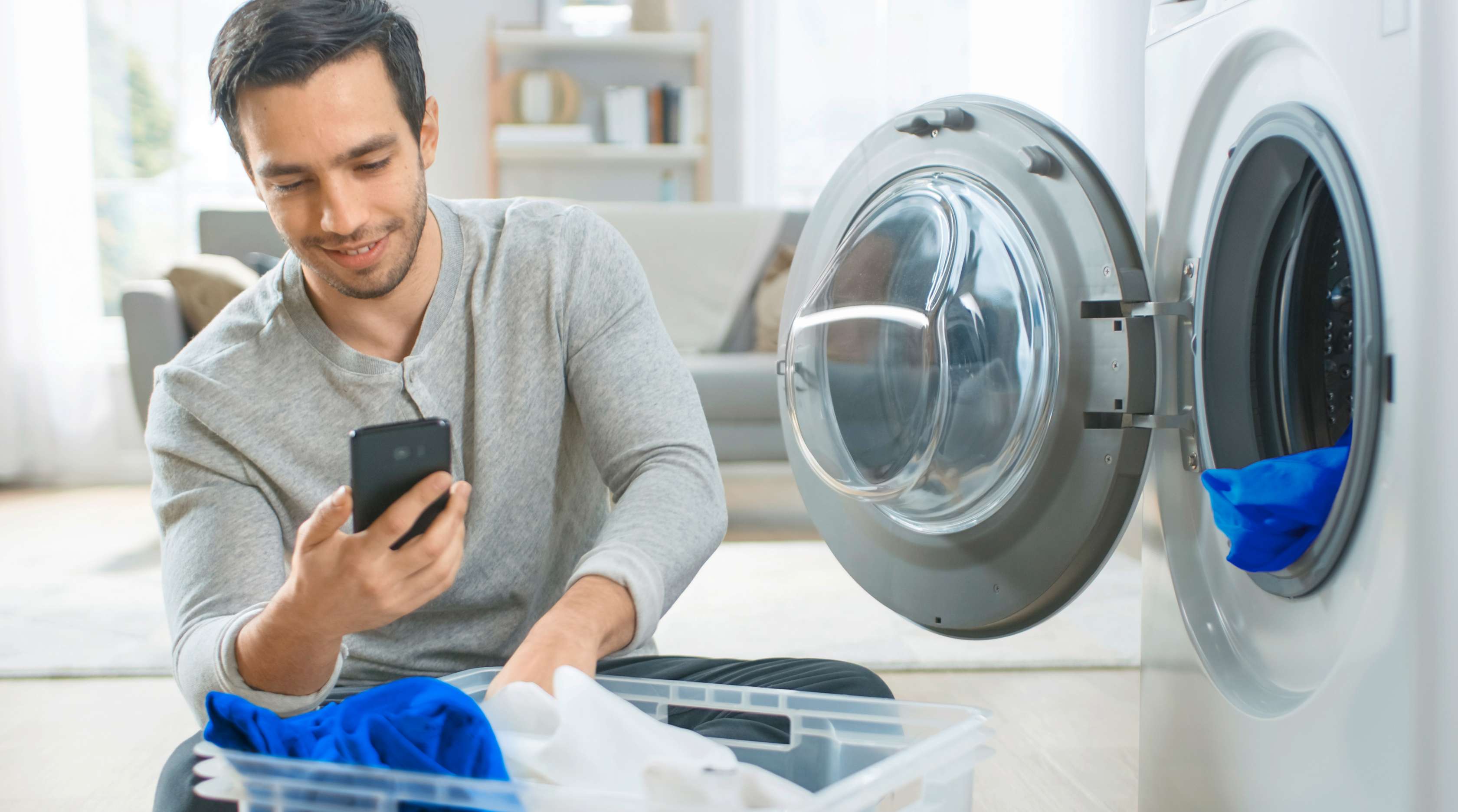 Hausrat-Haftpflicht-Kombi: Ein junger Mann sitzt mit Wäsche vor einer offenen Waschmaschine