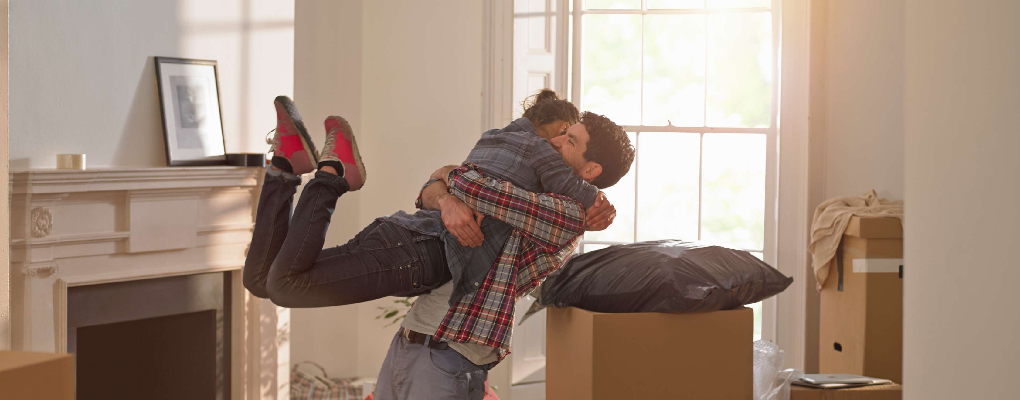 Junge Frau springt einem Mann in die Arme, um sie herum sind Kartons in einer Wohnung