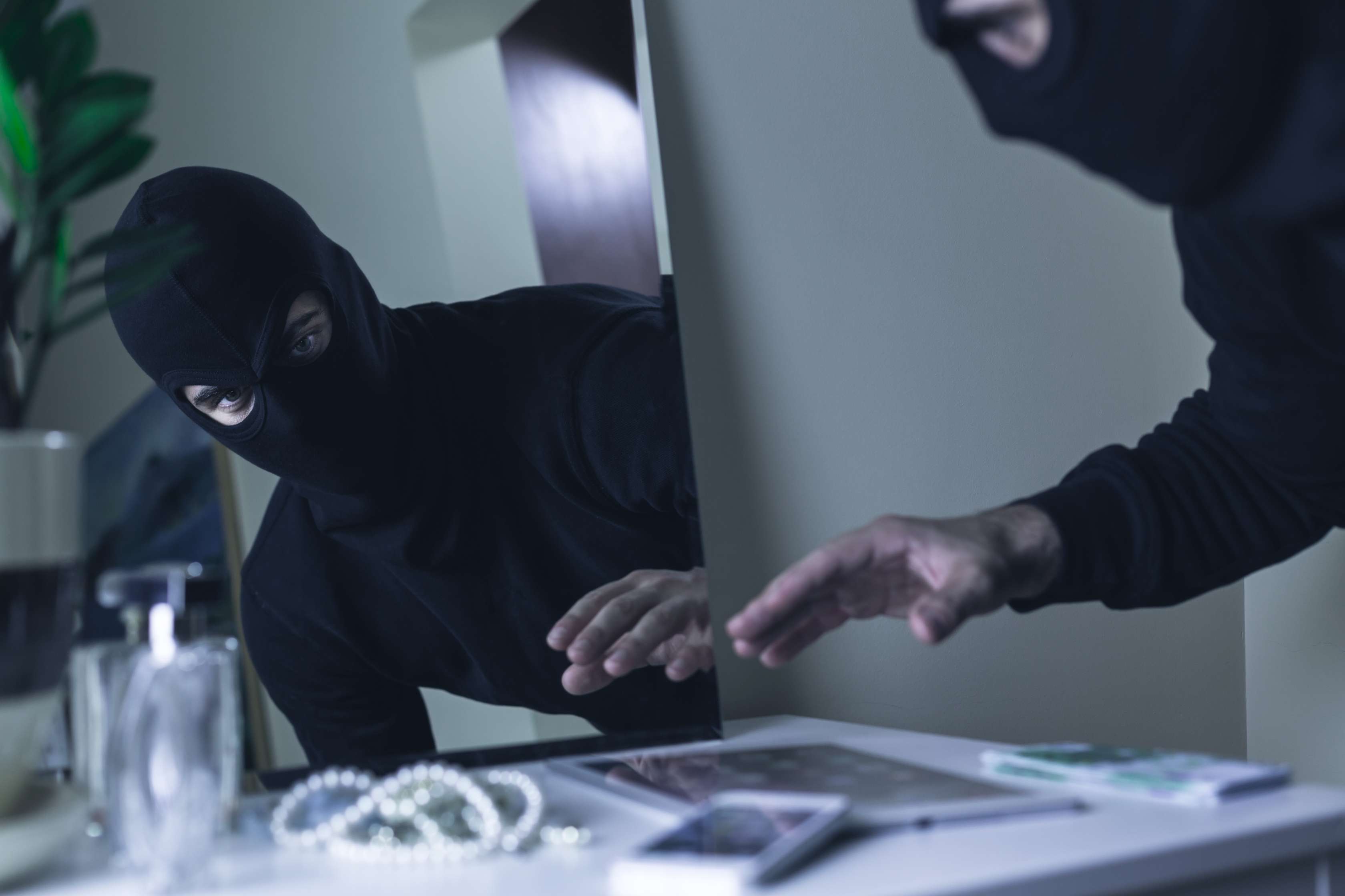 Maskierter Einbrecher greift in einer Wohnung nach Wertgegenständen.