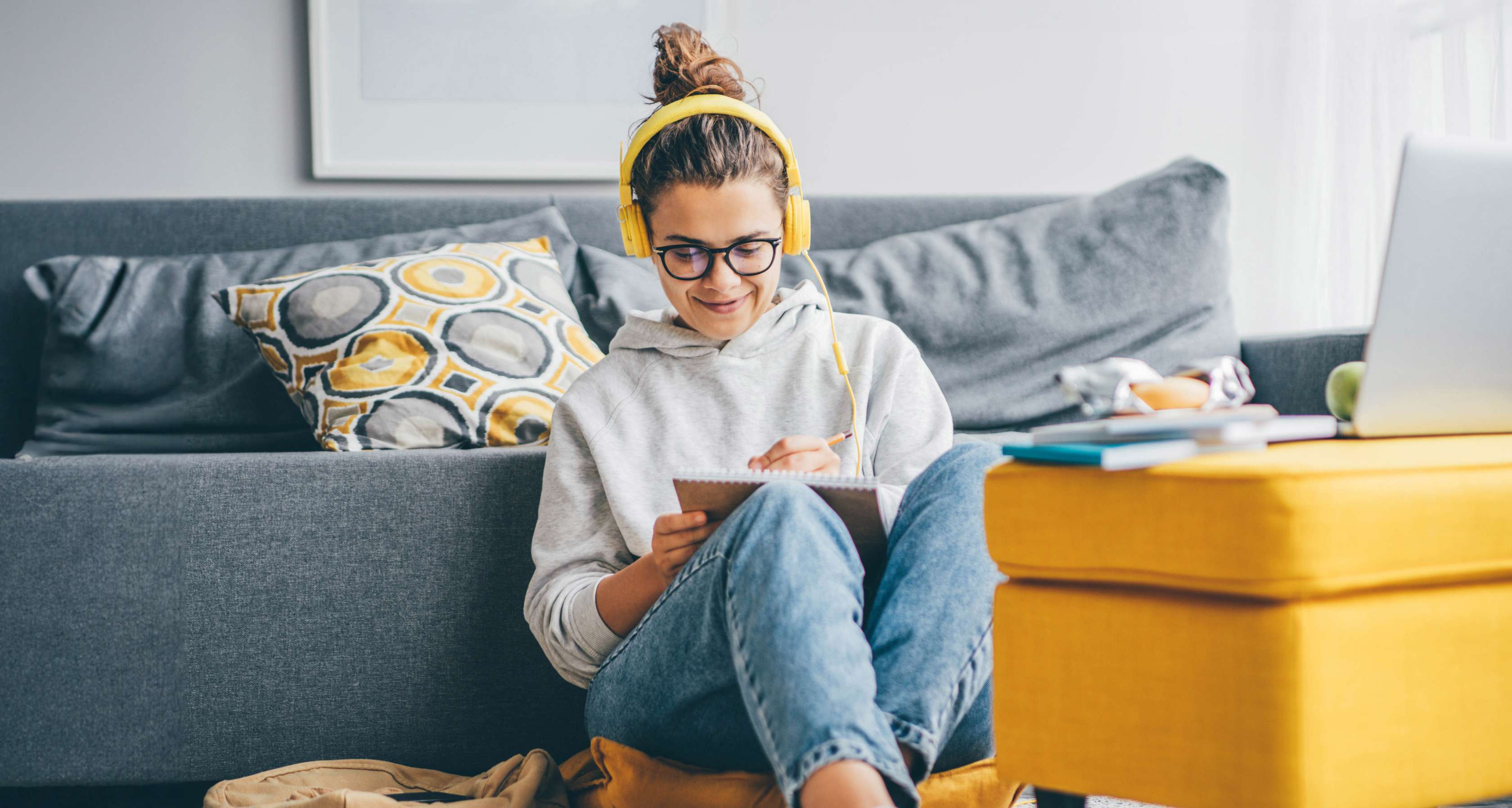 Hausratversicherung für Studenten: Studentin sitzt in eigener Wohnung und arbeitet mit Studienmaterialien.