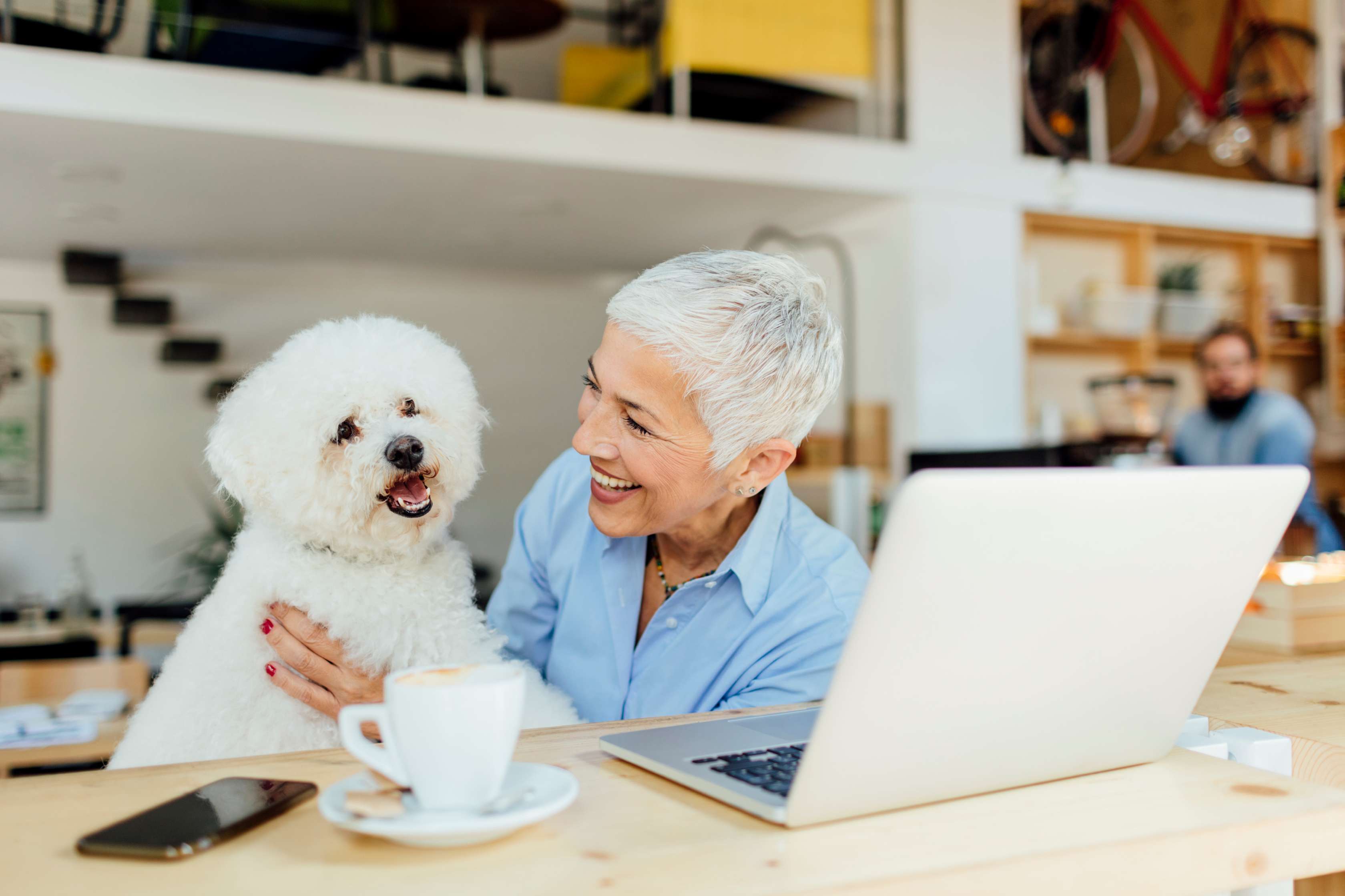 Frau sitzt mit weißem Hund vor einem Laptop